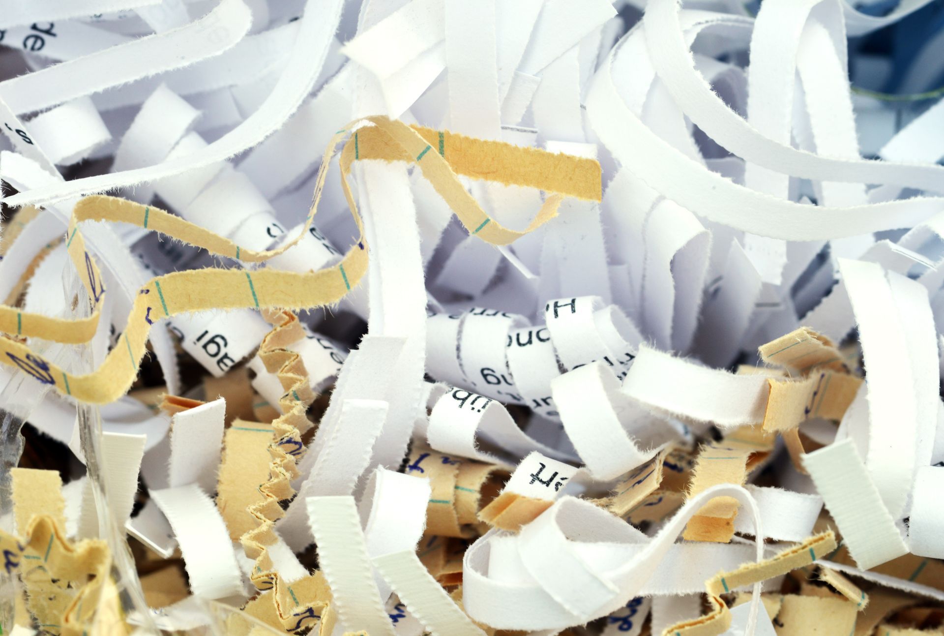 Des bouts de papier déchiquetés : des bandes blanches et beiges, certaines enroulées, remplissent une poubelle ; sécurité.