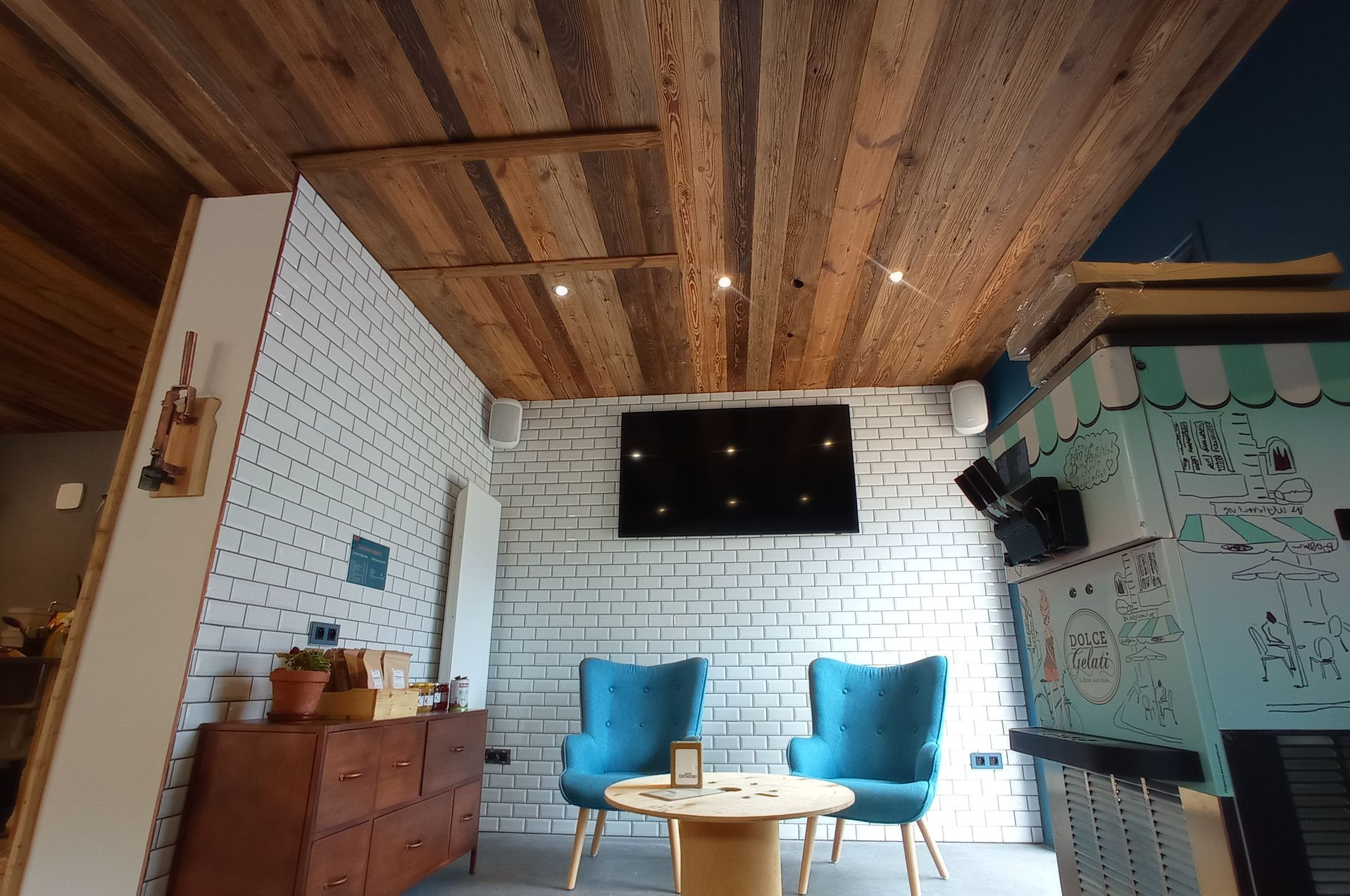 Salon rénové avec spots allumés sur un plafond en bois, deux fauteuils bleus et table ronde