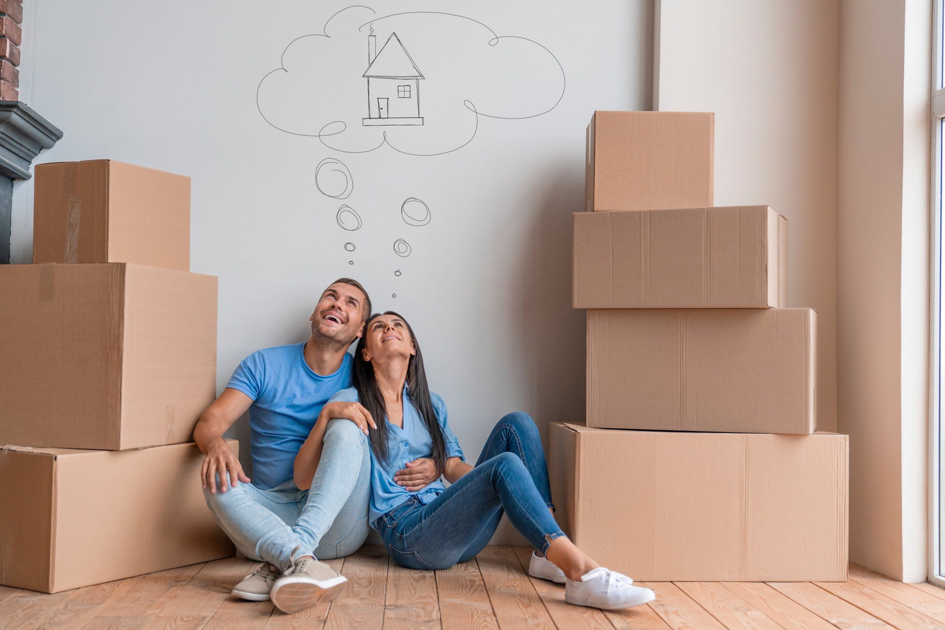 Couple souriant entouré de cartons lève la tête vers un dessin de maison dans une bulle de pensée