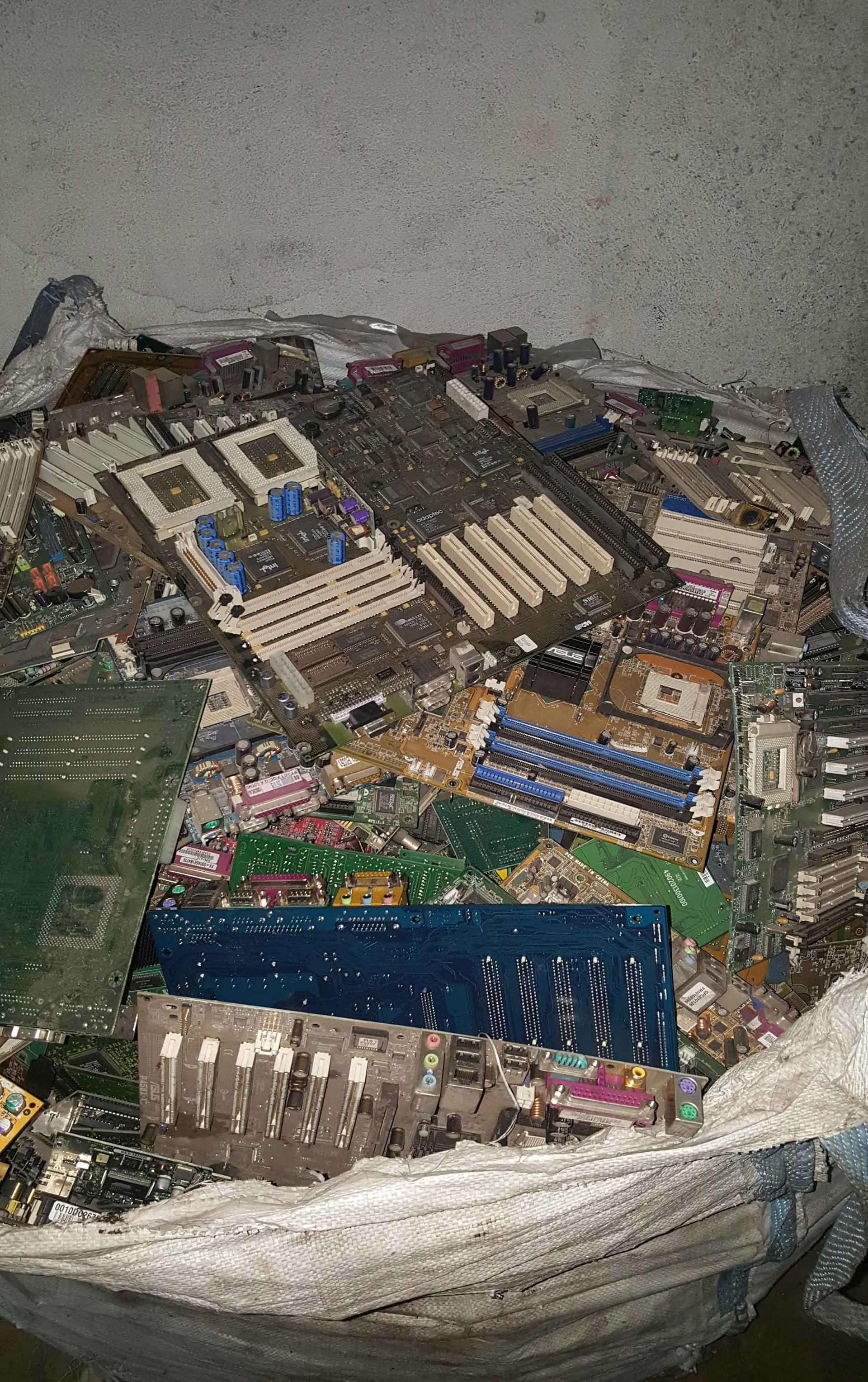 Pilha de placas de circuito descartadas, de vários tamanhos e cores, dentro de um contêiner branco.