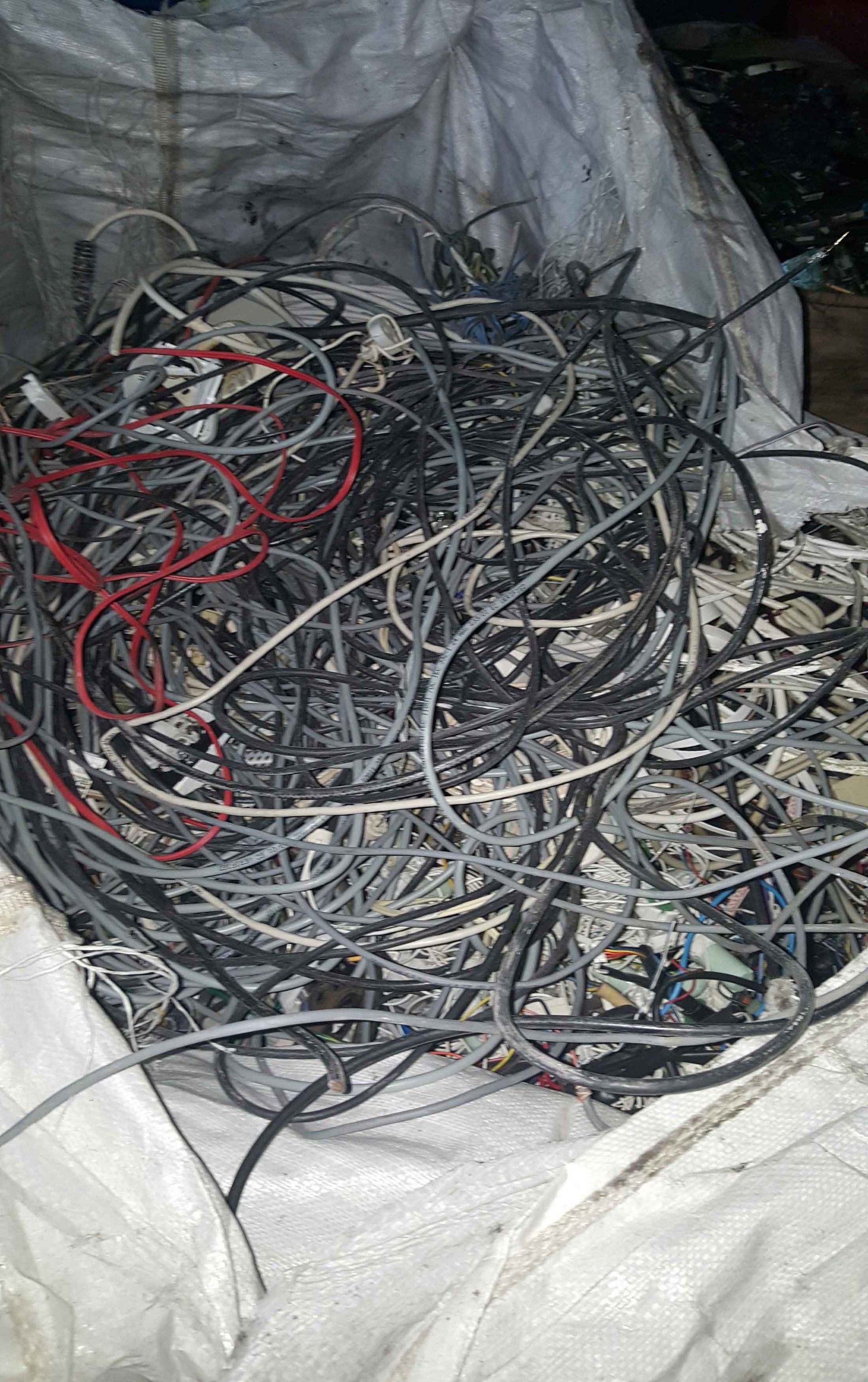 Emaranhado de fios elétricos misturados, principalmente cinza e preto, dentro de um saco branco.