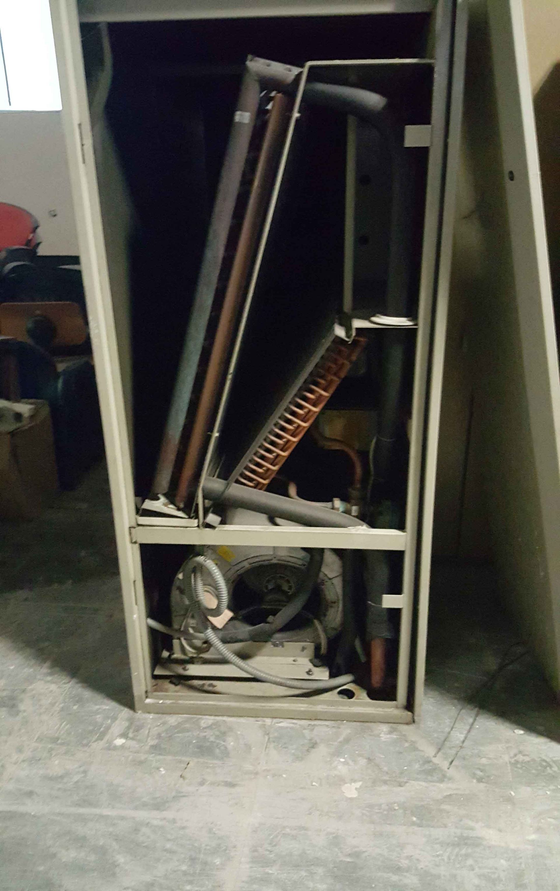 Unidade de climatização aberta com serpentinas de cobre e ventilador.