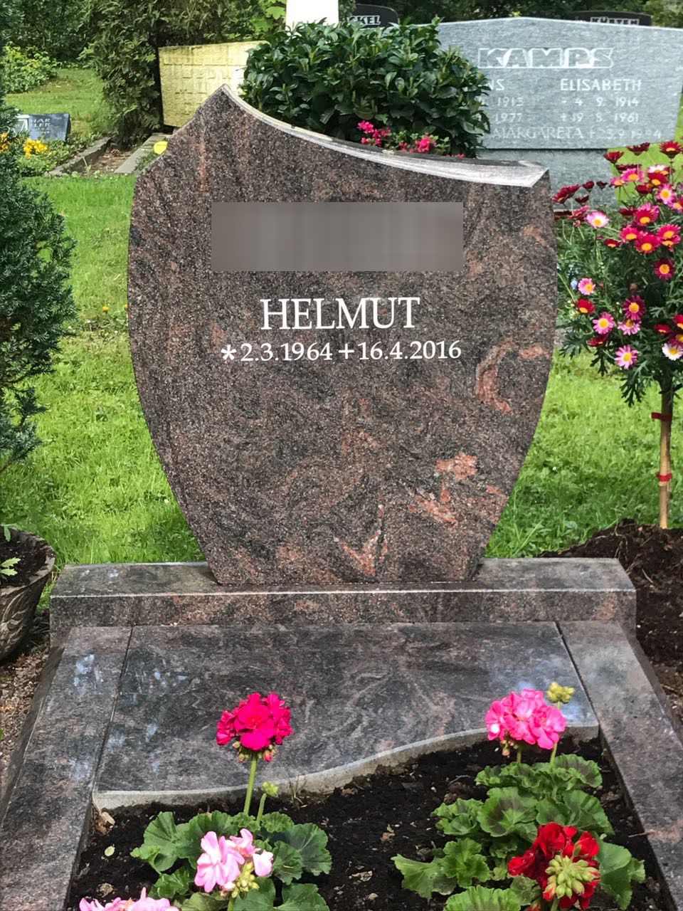 Ein Grabstein mit Blumen davor auf einem Friedhof.
