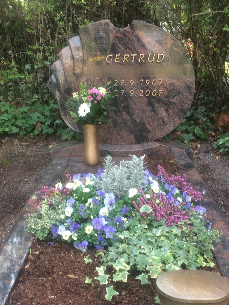 Ein Grab mit Blumen und einer Blumenvase darauf.