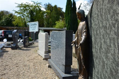 Eine Statue von Jesus lehnt an einer Mauer auf einem Friedhof