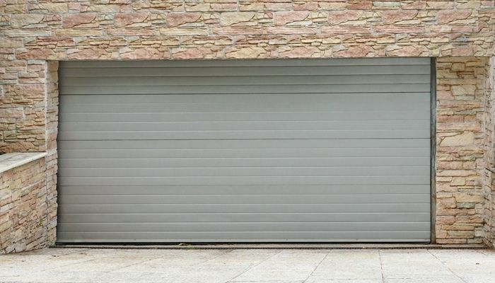 Una puerta de garaje gris está frente a una pared de ladrillos.