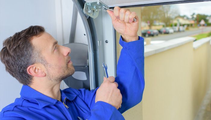 Un hombre está arreglando una puerta de garaje con una llave.