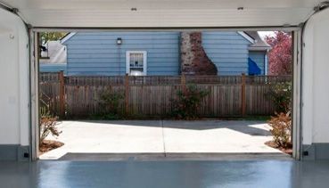 Una puerta de garaje está abierta a una casa azul con una valla al fondo.