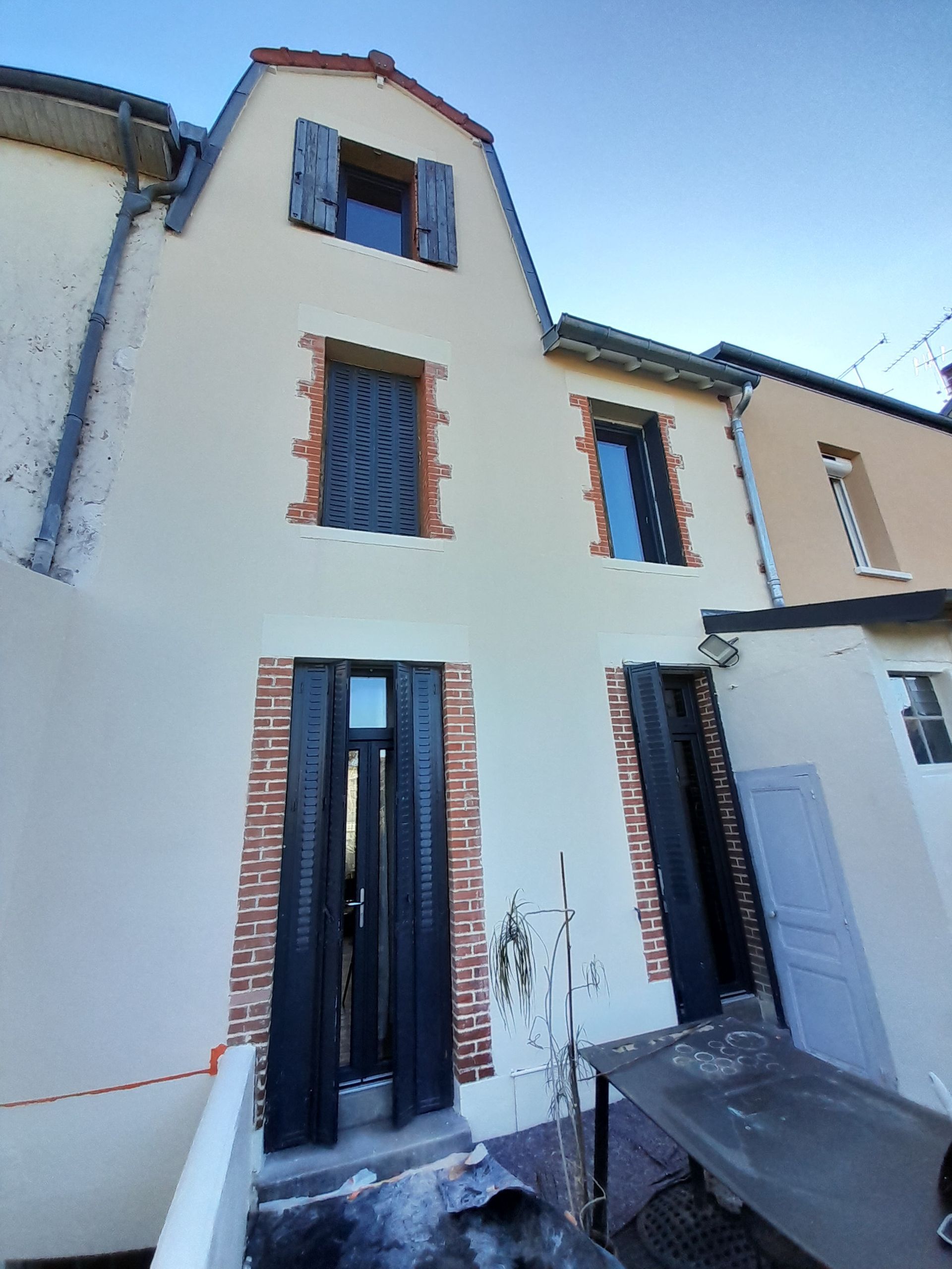 Rangée de maisons étroites en stuc, aux volets bleus et aux ornements en briques rouges, dans une rue ensoleillée