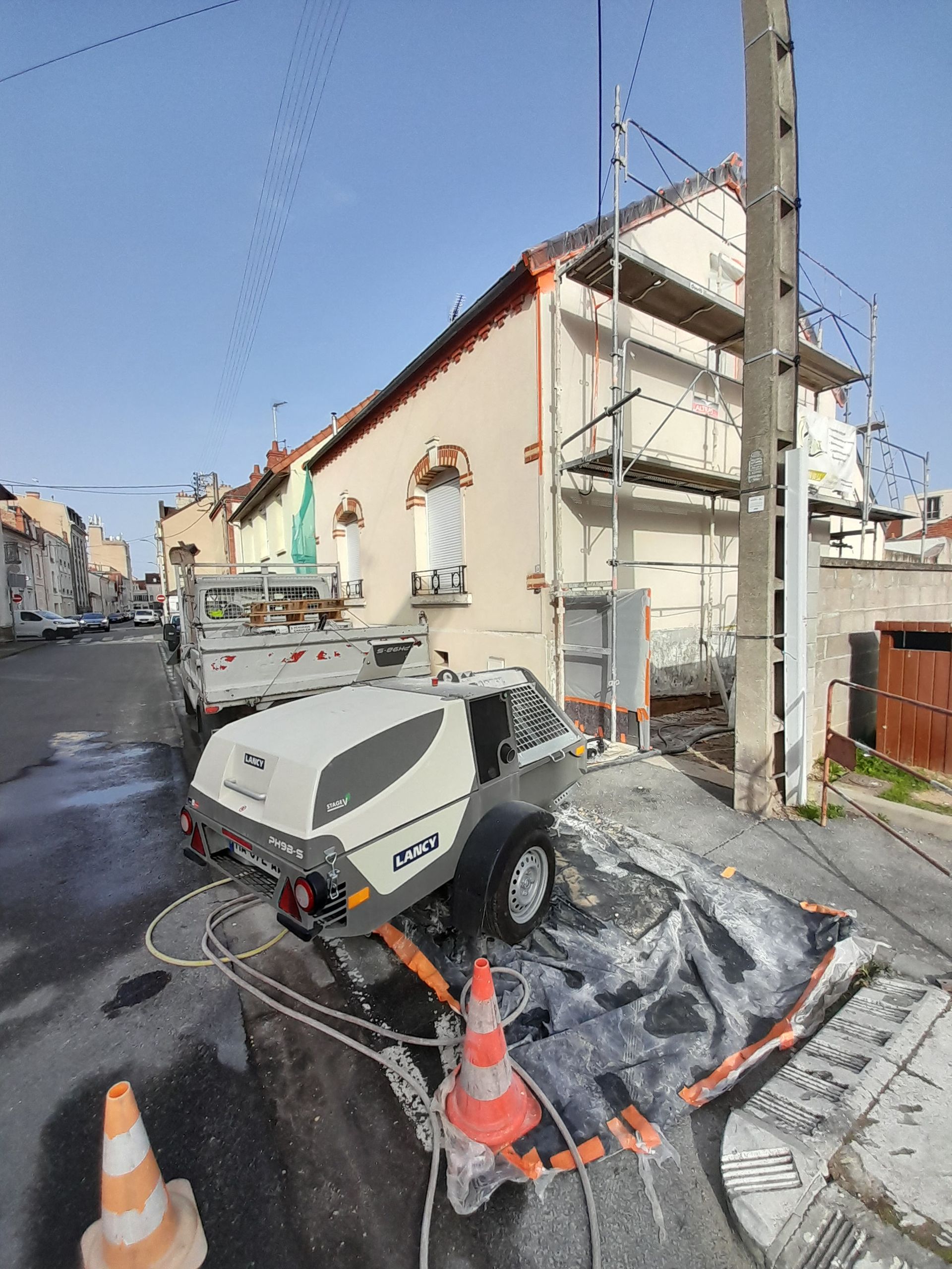 Une personne nettoie un mur en stuc au nettoyeur haute pression depuis un échafaudage, créant un jet d'eau.