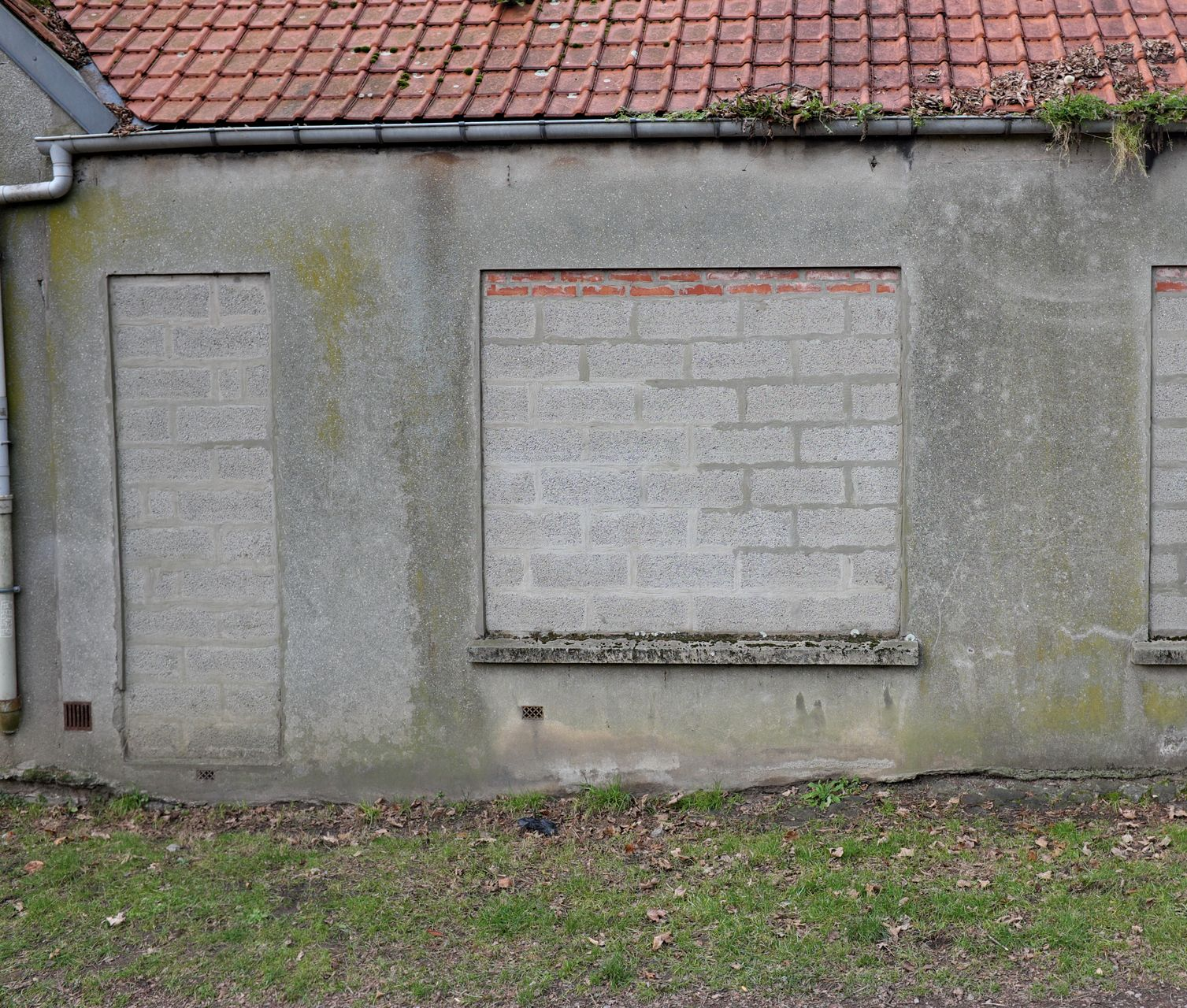 Bâtiment délabré, avec une porte et une fenêtre condamnées, un toit de tuiles et boiseries moussues.
