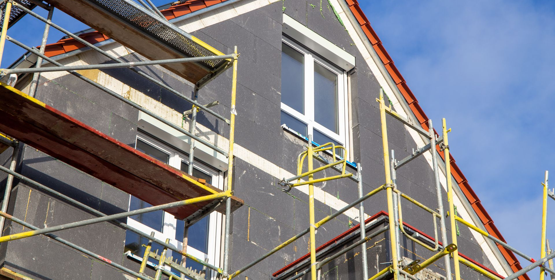 Extérieur du bâtiment en construction ; échafaudages, bardage, fenêtres, toit.