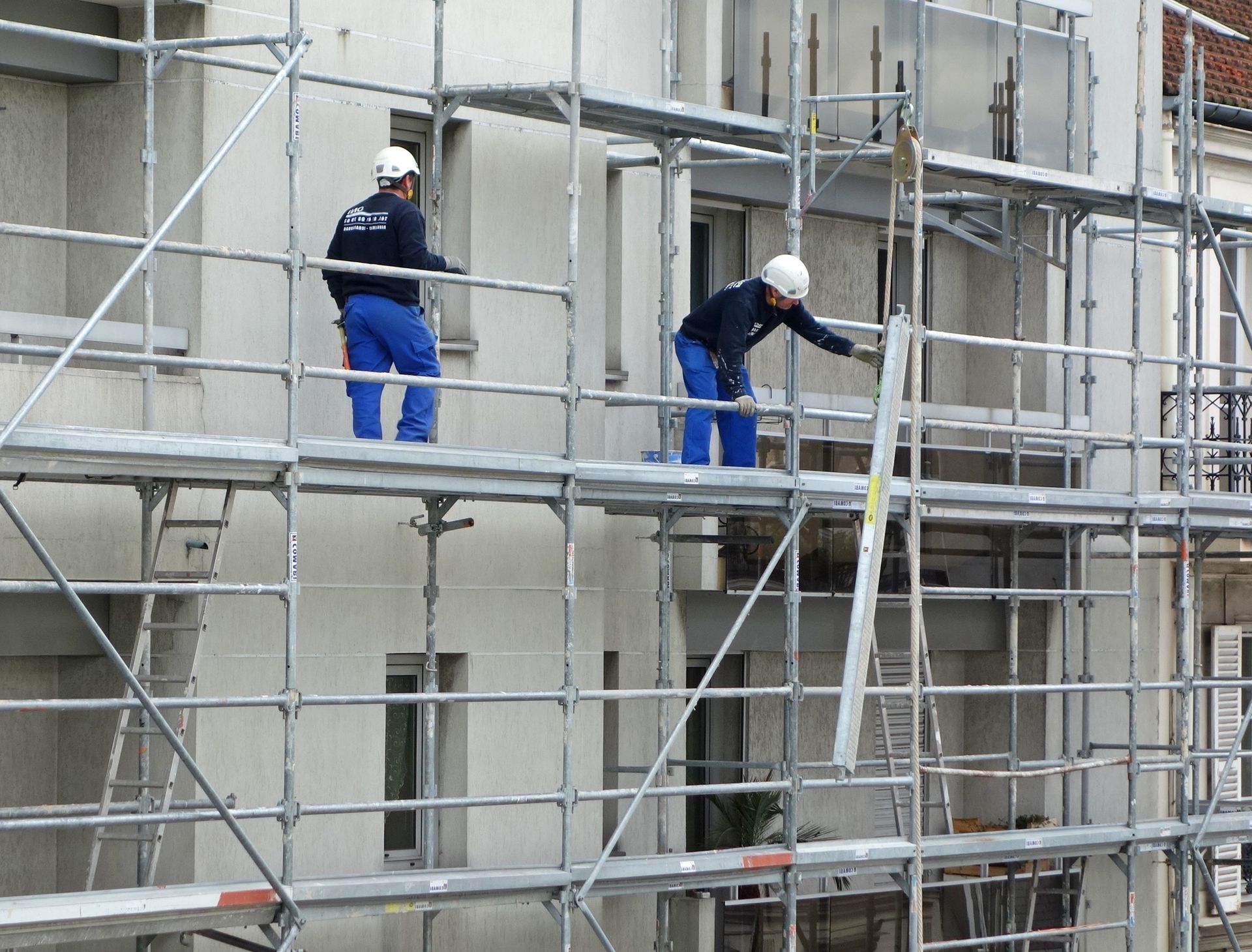 Deux ouvriers du bâtiment sur un échafaudage, en train de réparer un immeuble.