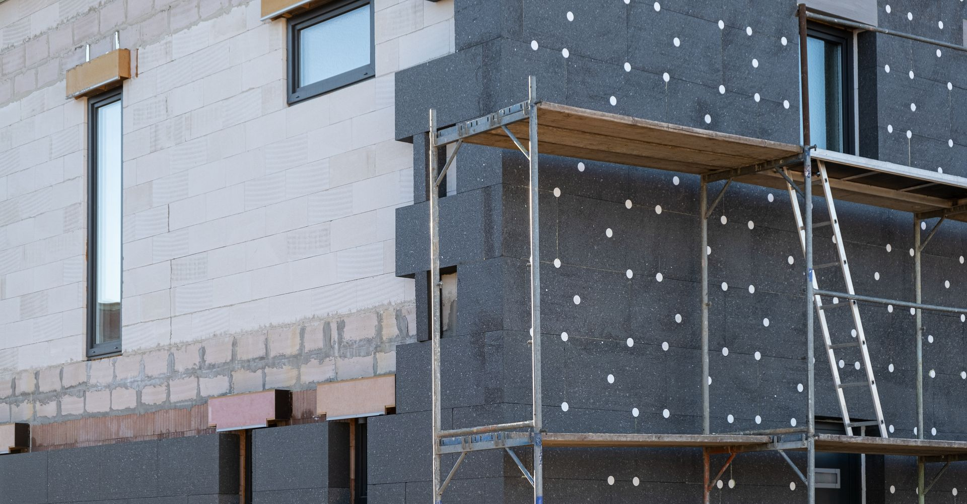 Mur extérieur en construction avec une isolation, un échafaudage et des fenêtres.