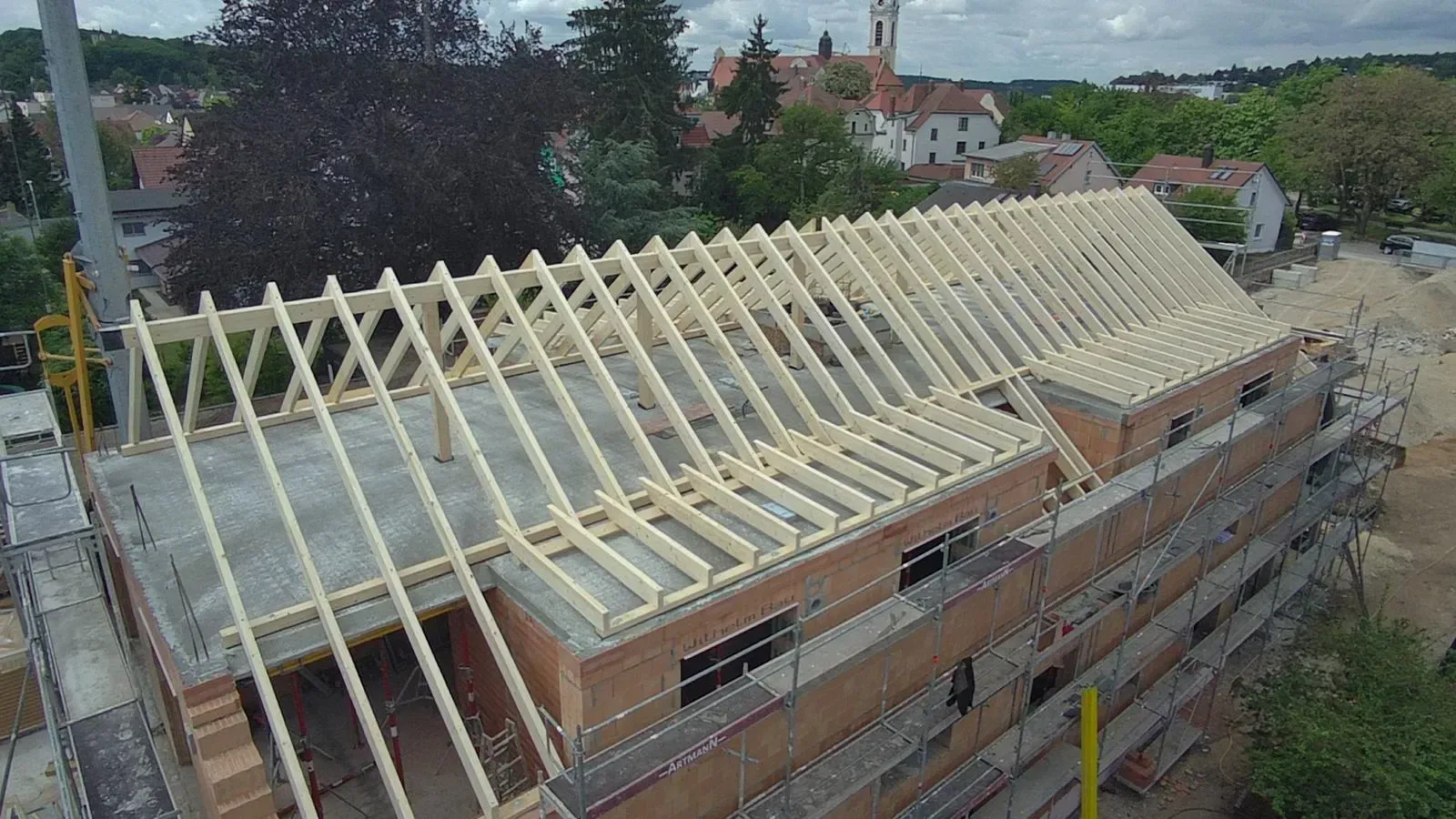 Im Bau befindliche Dachkonstruktion eines Backsteingebäudes, wobei die hellen Holzsparren auf einem geneigten Dach sichtbar sind.