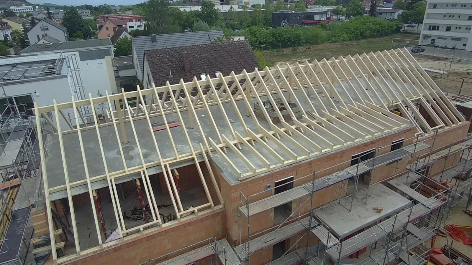 Dachkonstruktion an einem Backsteingebäude mit freiliegenden Holzsparren und umliegenden Wohnhäusern.