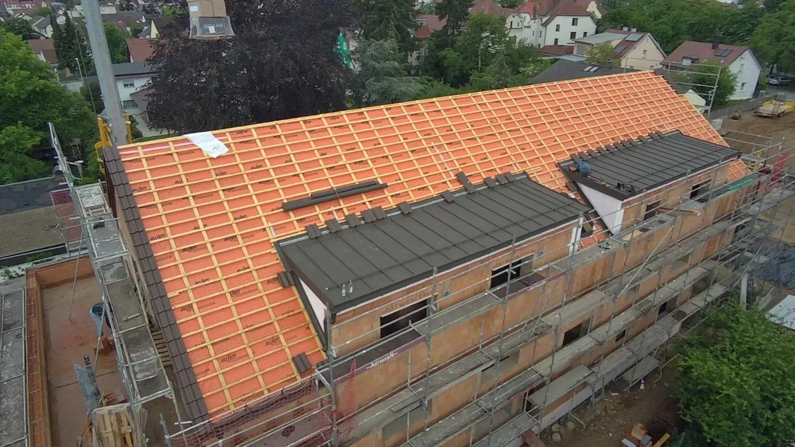 Luftaufnahme eines im Bau befindlichen Gebäudes mit einem großen orangefarbenen Ziegeldach und freiliegenden Ziegelwänden.