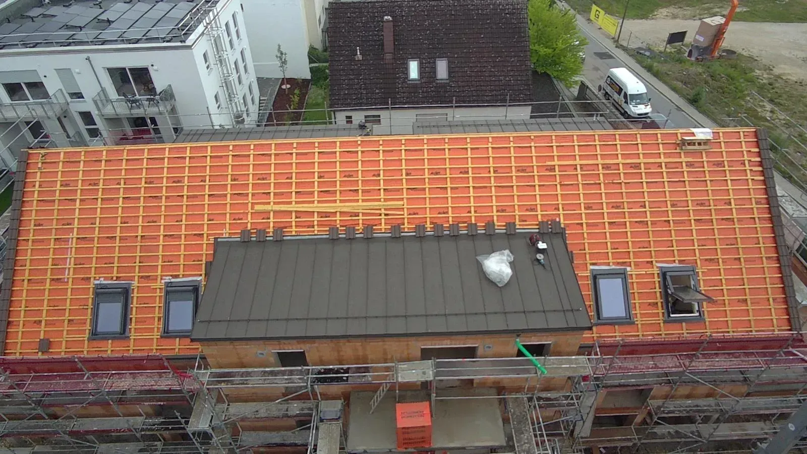 Das Dach befindet sich im Bau und weist eine orangefarbene Dämmung, einen grauen mittleren Dachabschnitt und ein umgebendes Gerüst auf.