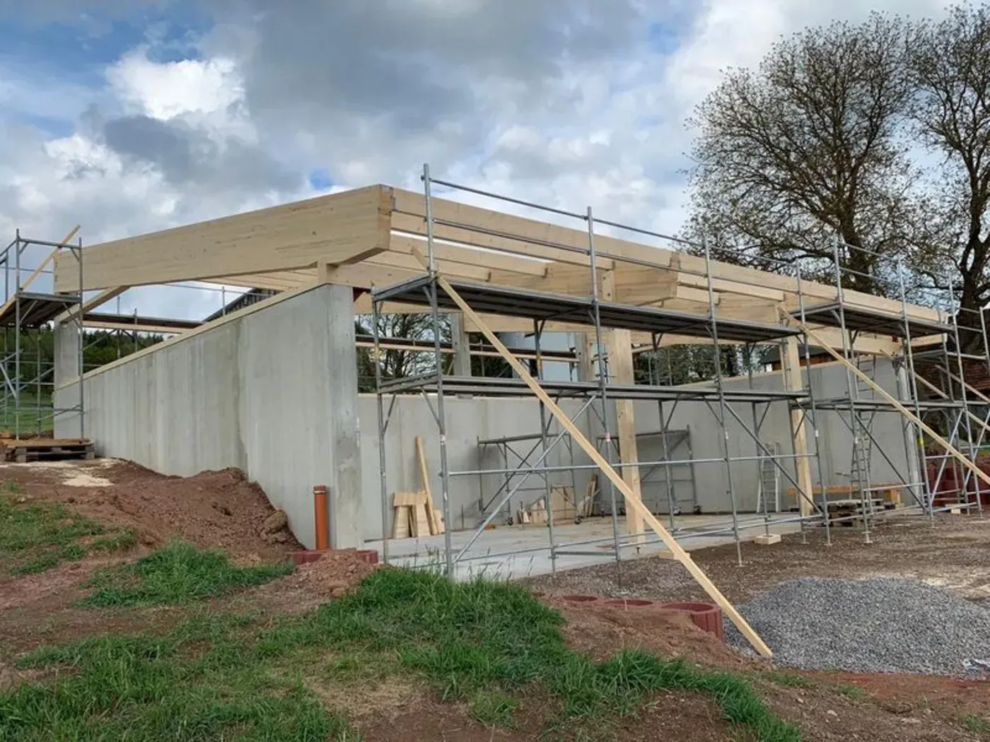 Ein teilweise errichtetes Haus mit hölzerner Dachkonstruktion, Metallverkleidung und Gerüst an einem bewölkten Tag