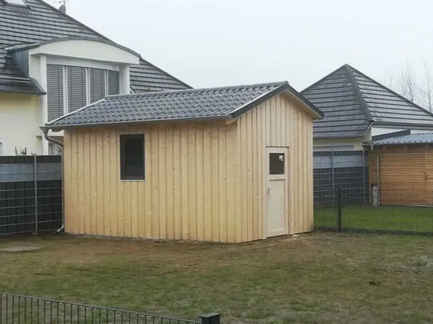 Kleiner beigefarbener Schuppen mit schrägem Dach in einem umzäunten Garten