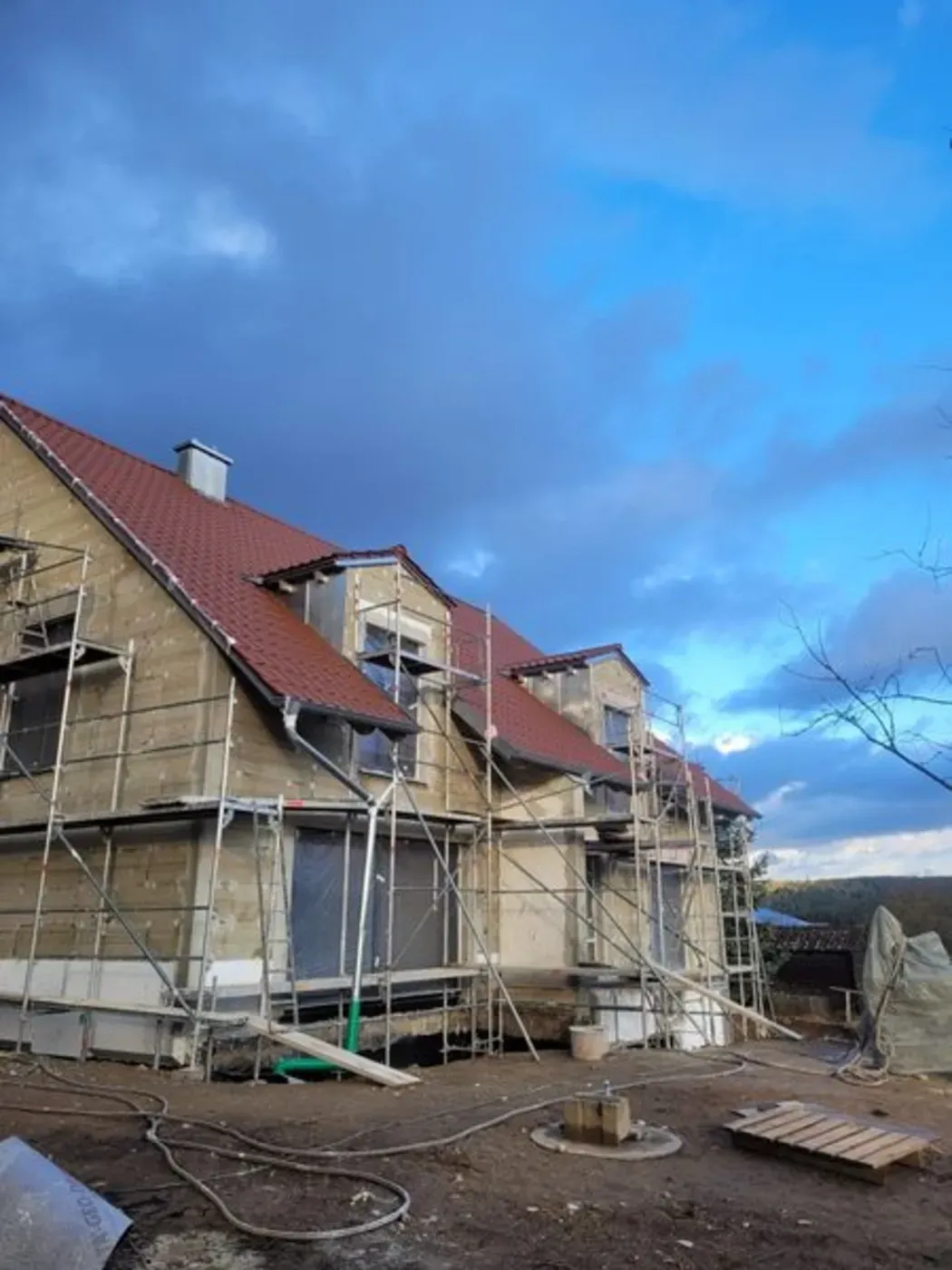 Haus im Umbau mit Gerüst, rotem Dach und blauem Himmel.