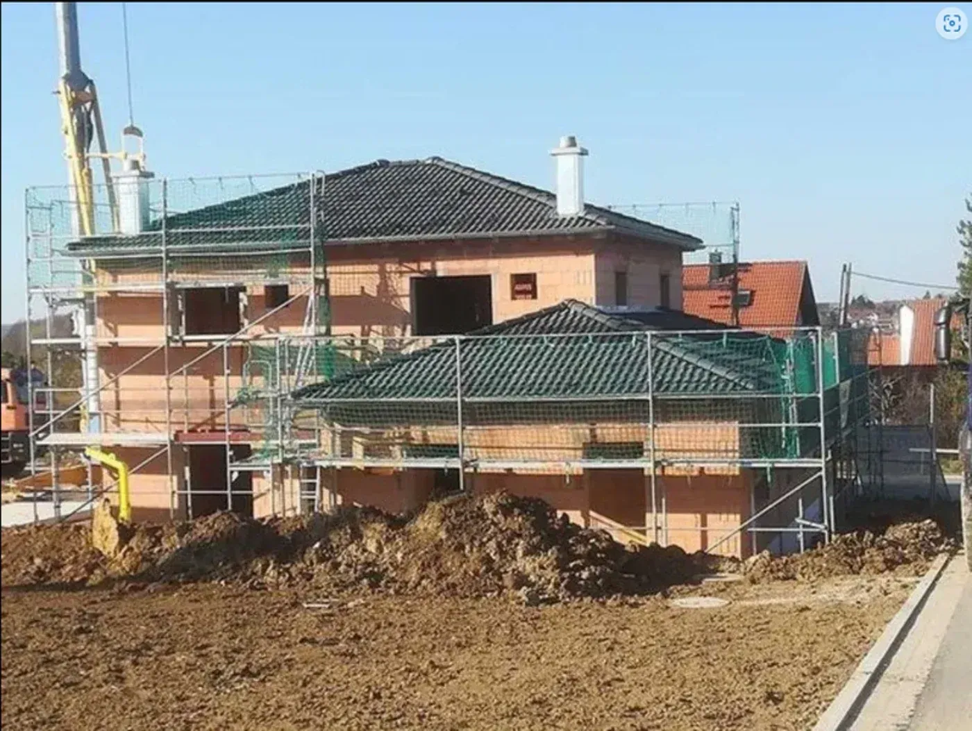 Haus im Bau mit Gerüst und Erde im Vordergrund unter klarem Himmel