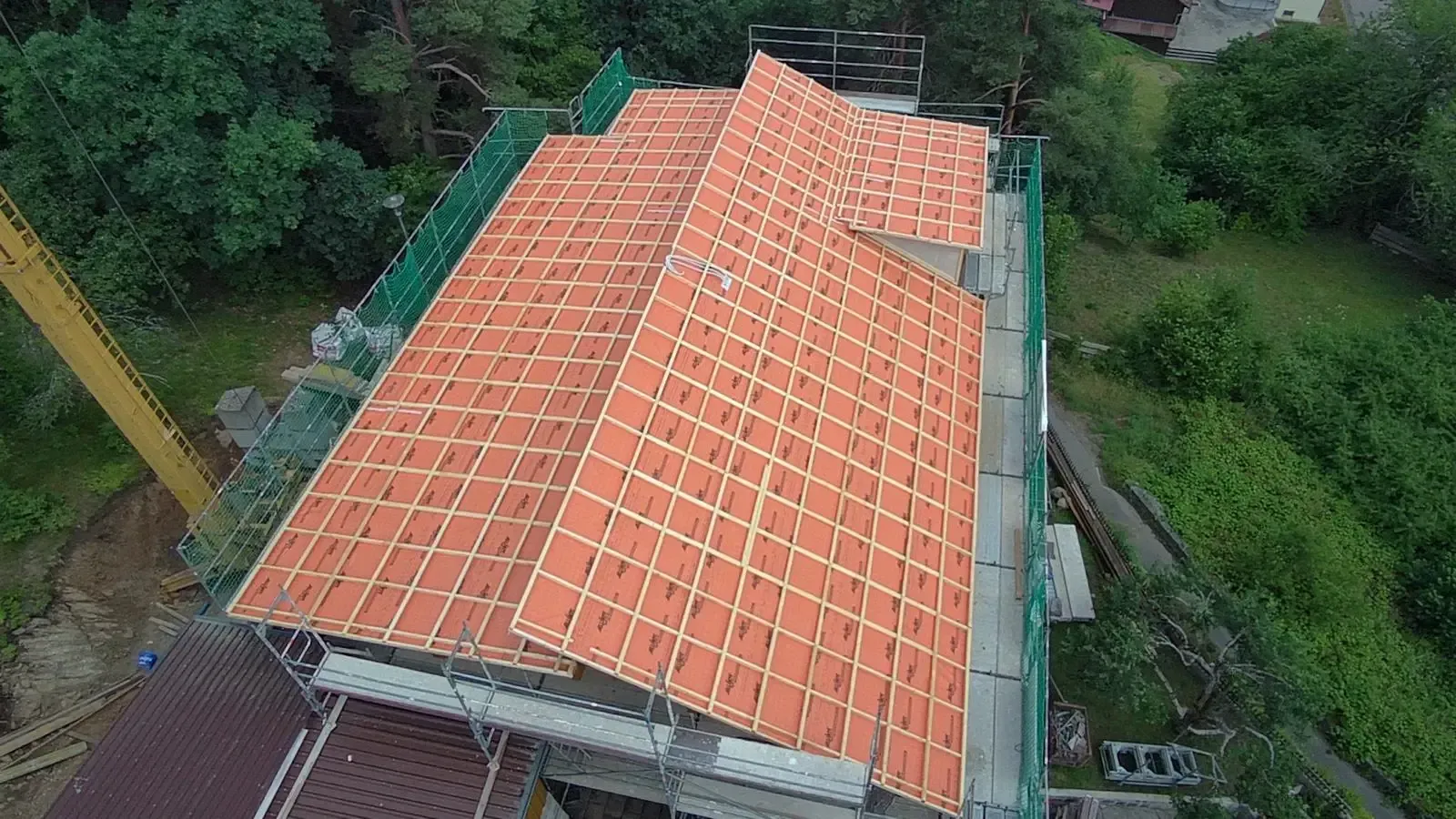 Luftaufnahme eines im Bau befindlichen Hausdachs mit orangefarbenen Ziegeln und umgebender Vegetation.