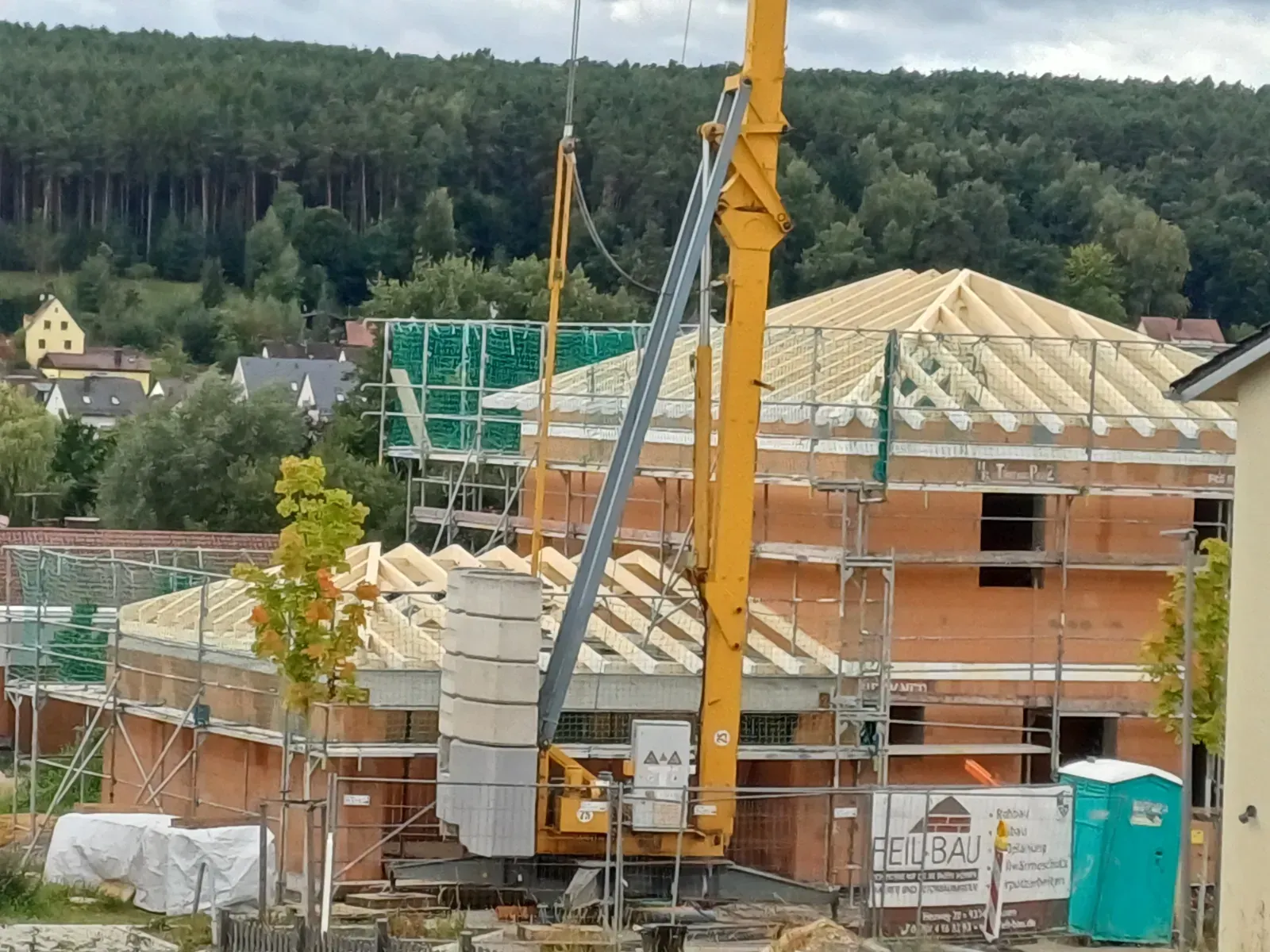 Baustelle mit gelbem Kran und Gerüst um unfertige Backsteinhäuser unter bewölktem Himmel
