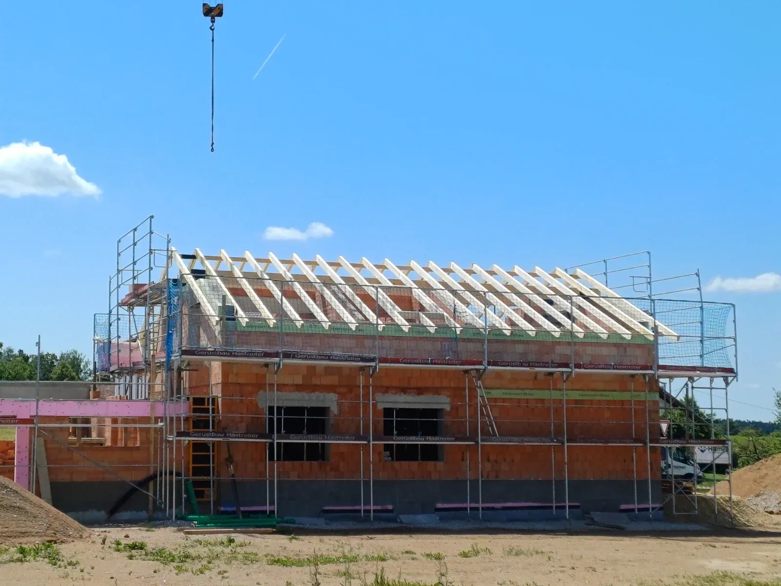 Haus im Bau mit Gerüst und unfertigem Dach unter blauem Himmel