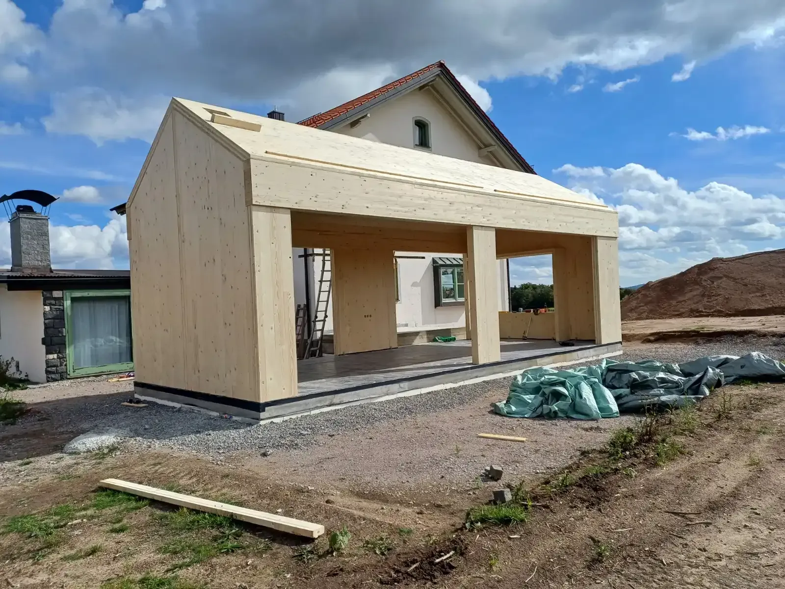 Teilweise errichtetes Haus mit Holzrahmen und überdachter Veranda unter bewölktem Himmel