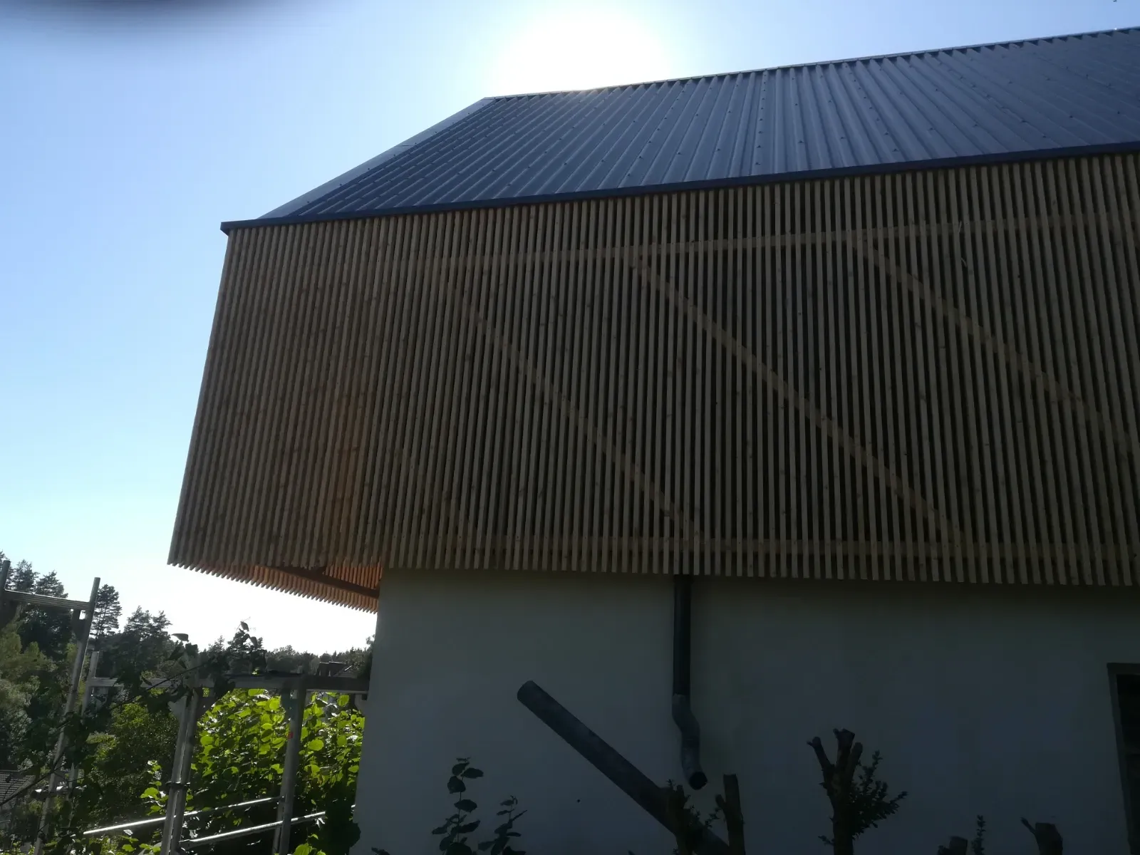 Sonnenbeschienenes Schrägdach über einem weißen Gebäude mit Bäumen und blauem Himmel