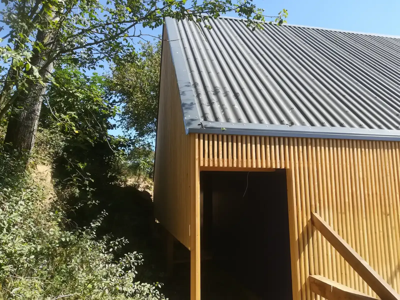 Kleine Holzhütte mit Wellblechdach neben Bäumen und Grün
