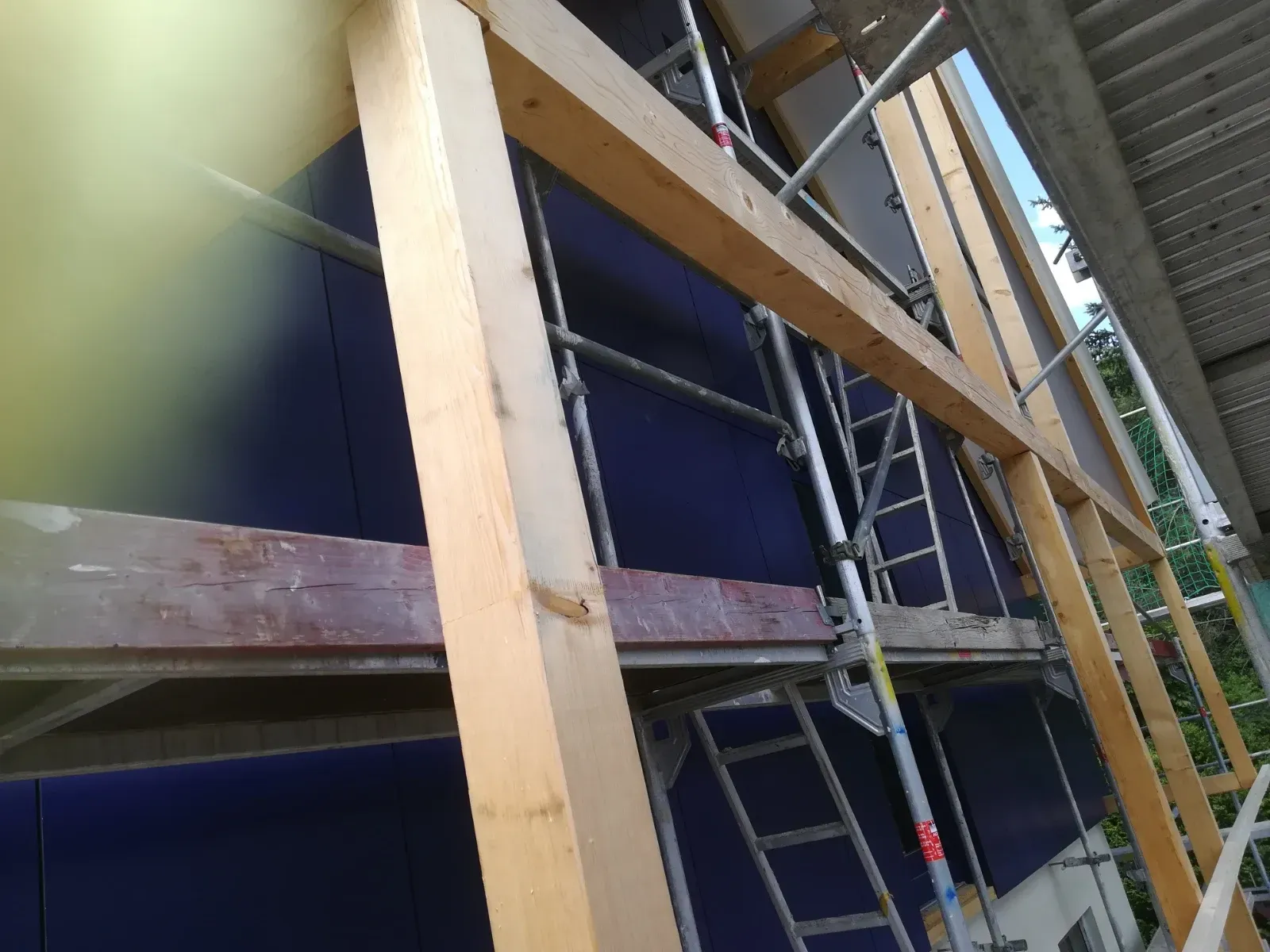 Leiter und Holzbalken vor einer blauen Wand auf einer Baustelle