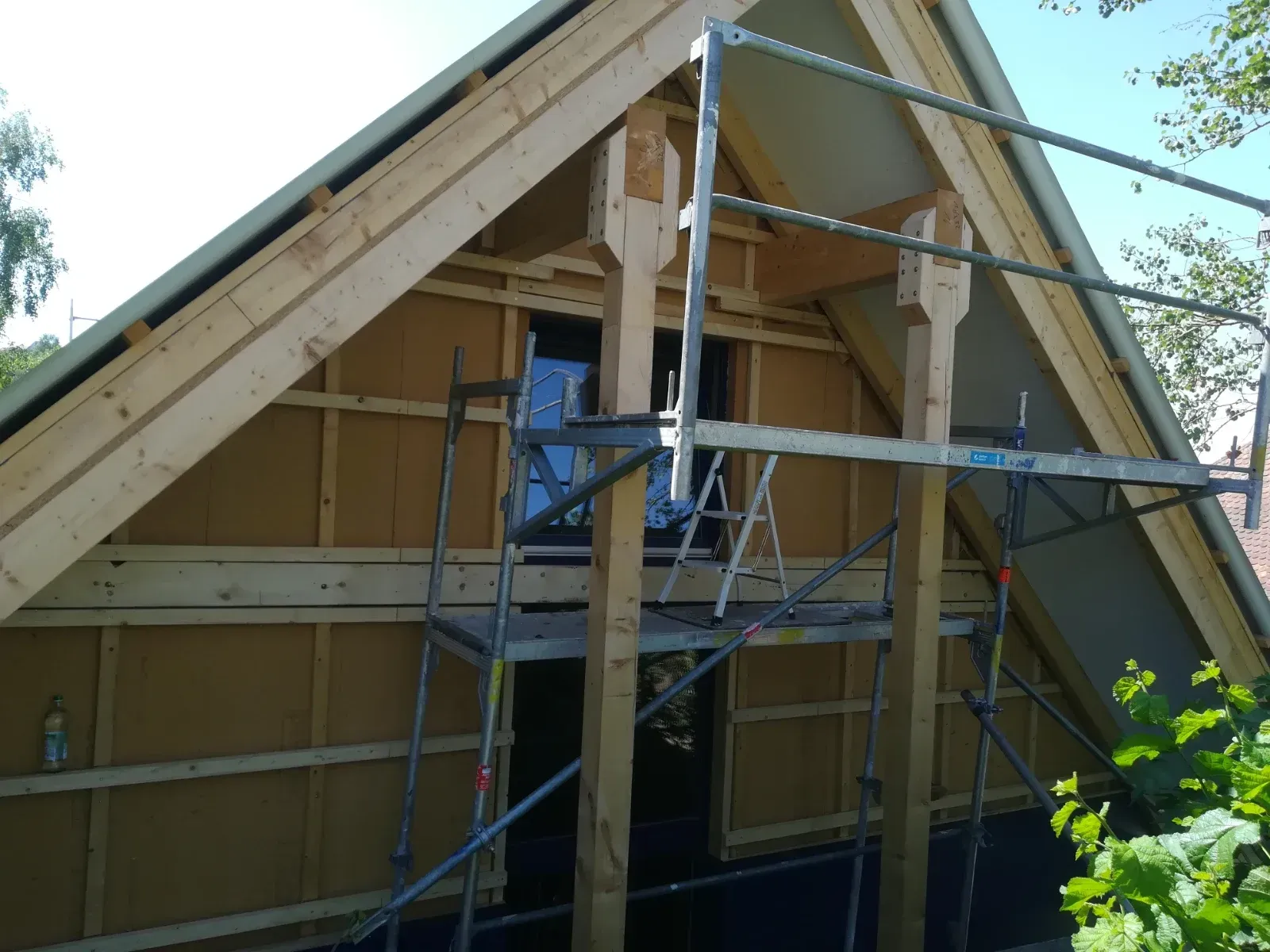 Ein Baugerüst umgibt ein im Bau befindliches Haus mit freiliegender Holzverkleidung und steilem Giebeldach.