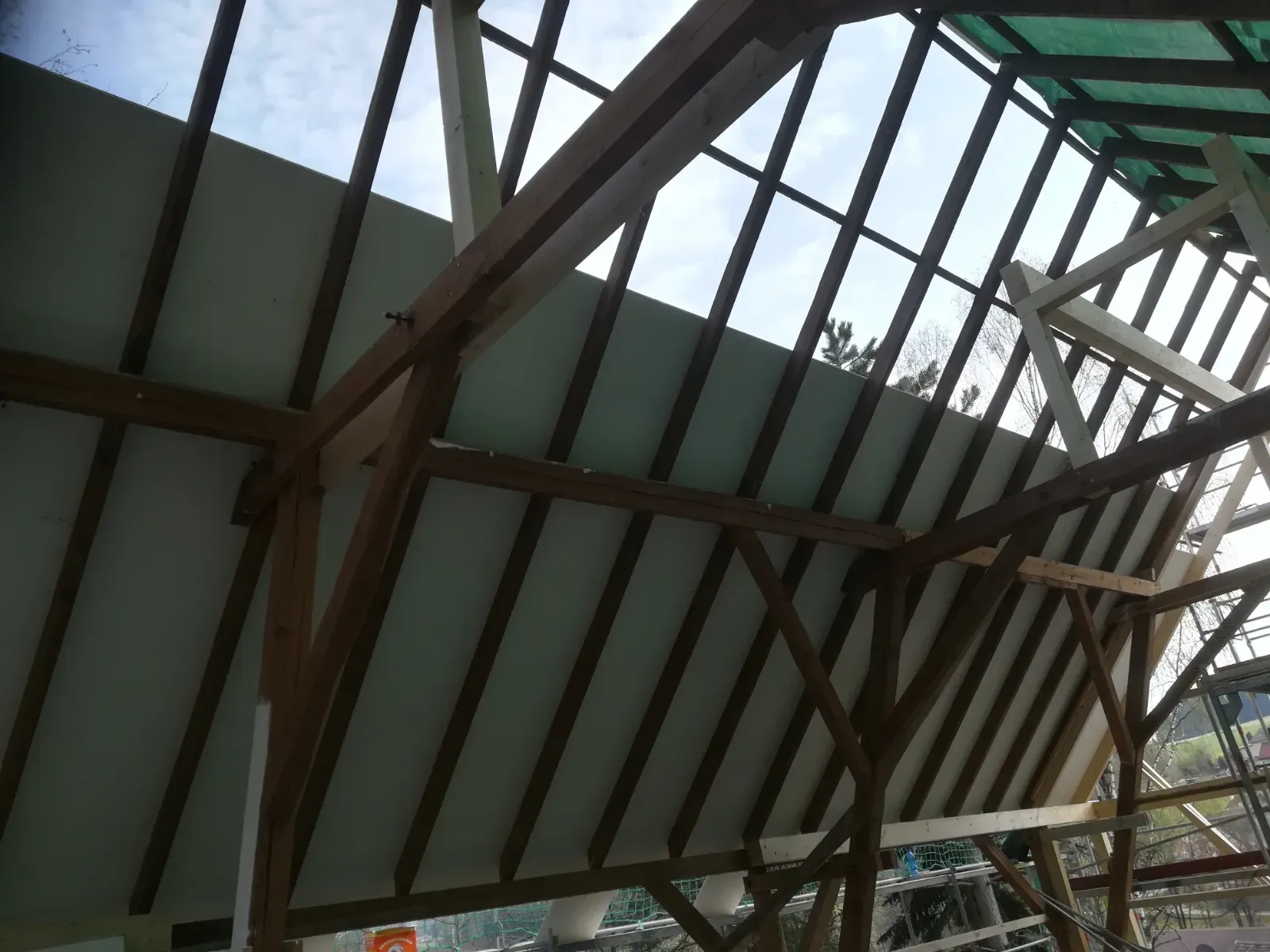 Dachkonstruktion mit grünen Paneelen und dunklen Holzbalken im Bau, von unten betrachtet