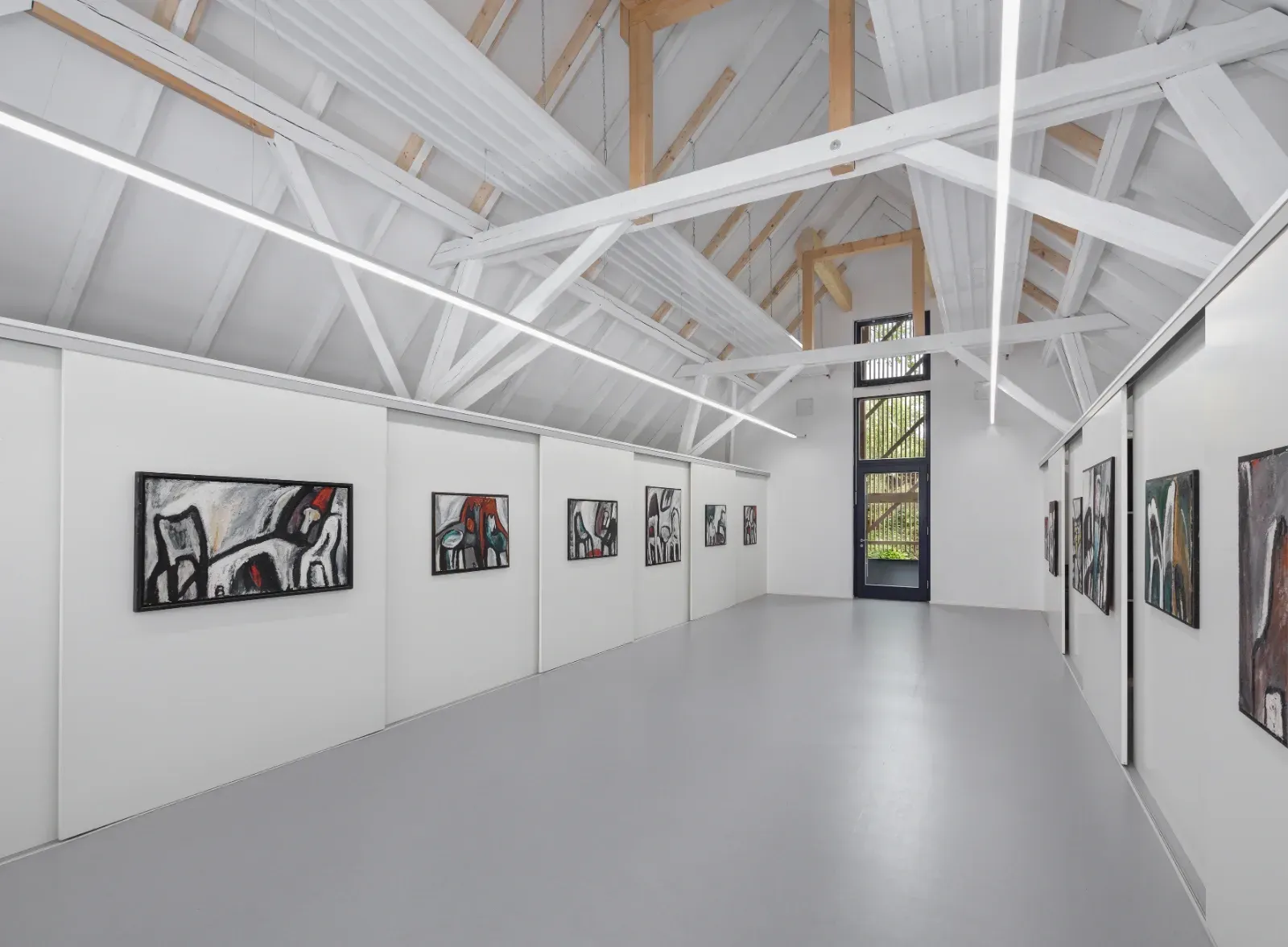 Helles Interieur der Kunstgalerie mit weißen Wänden, freiliegenden Balken und gerahmten Gemälden an beiden Seiten.