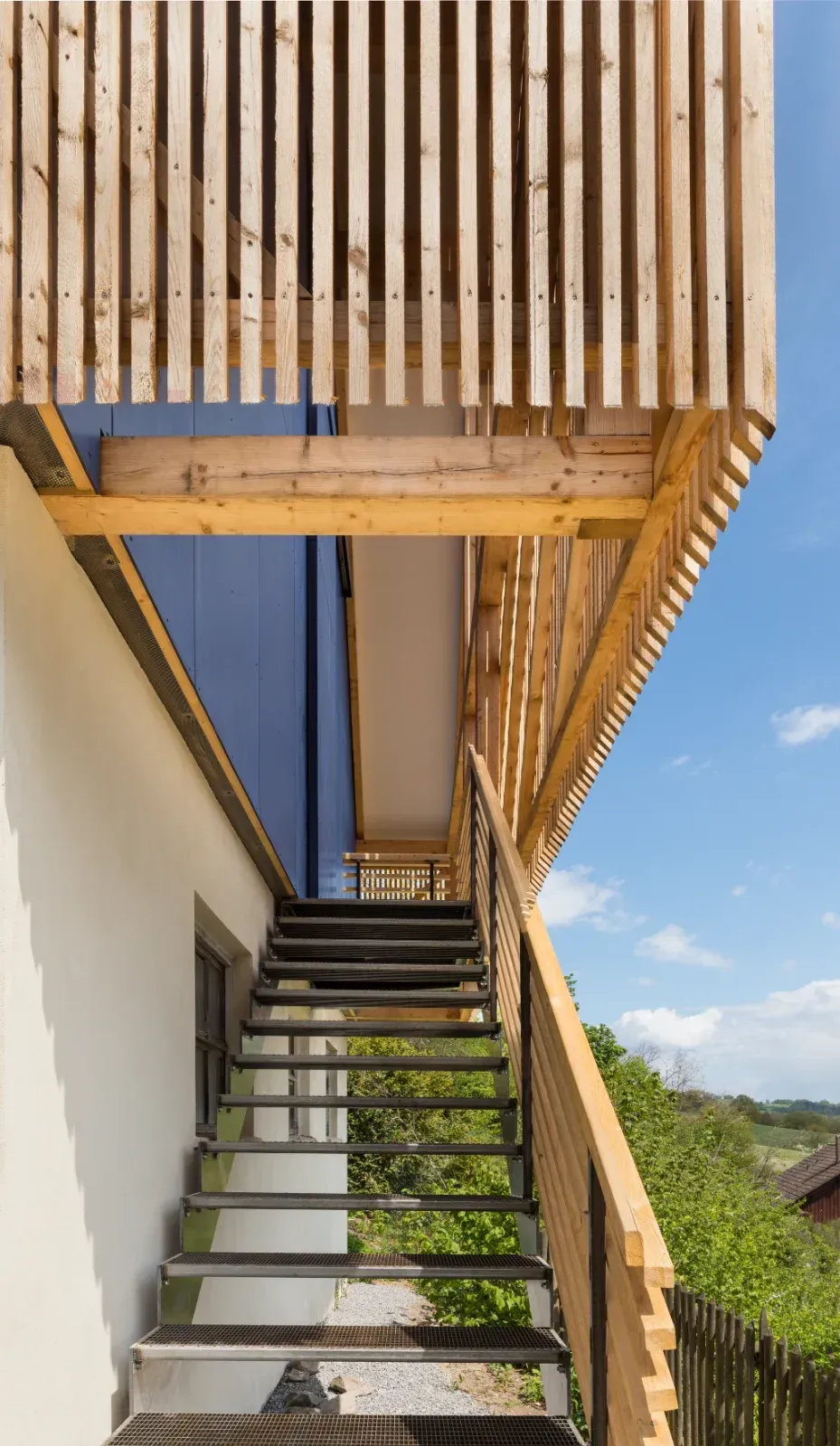 Außentreppe neben einem modernen Haus mit Holzlatten und blauem Himmel darüber