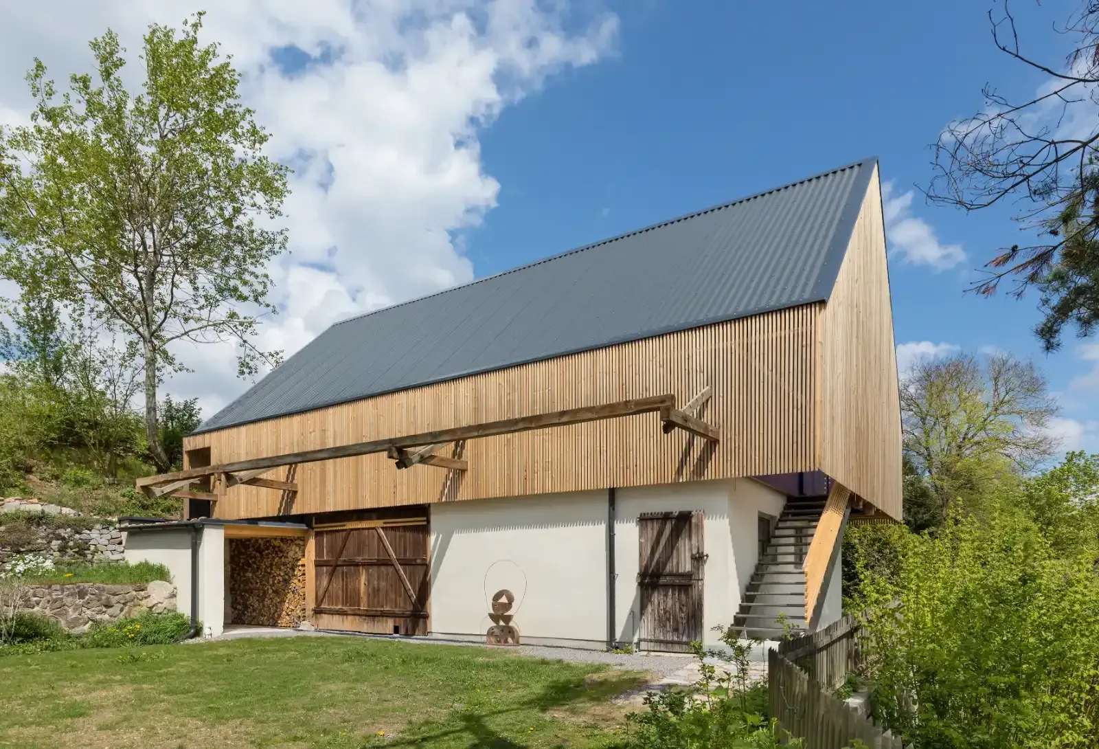 Modernes Haus im Scheunenstil mit Holzverkleidung, schrägem Metalldach und Außentreppe in einem grasbewachsenen Garten