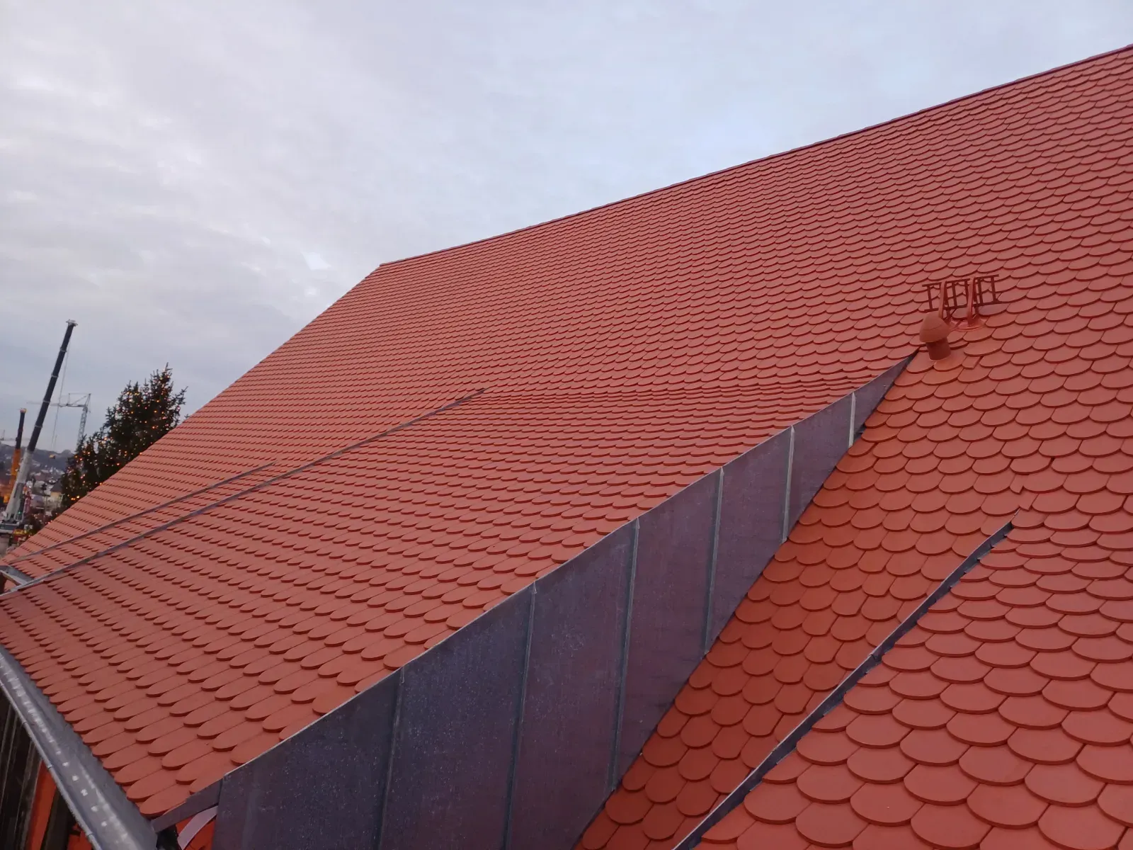 Rotes Ziegeldach mit großem dreieckigem Oberlicht unter einem bewölkten Himmel