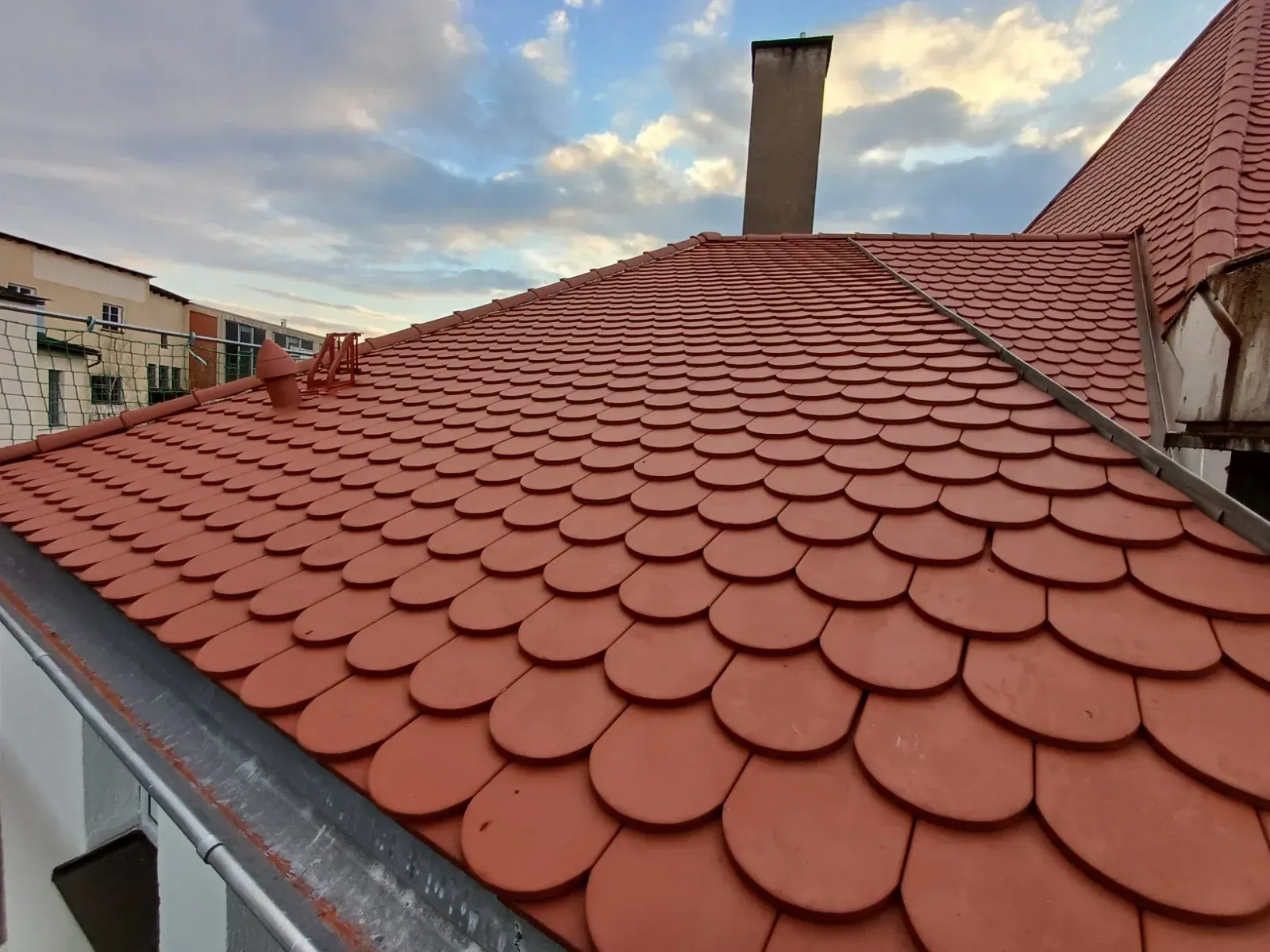 Rotes Ziegeldach mit Schornstein unter bewölktem Himmel in der Abenddämmerung