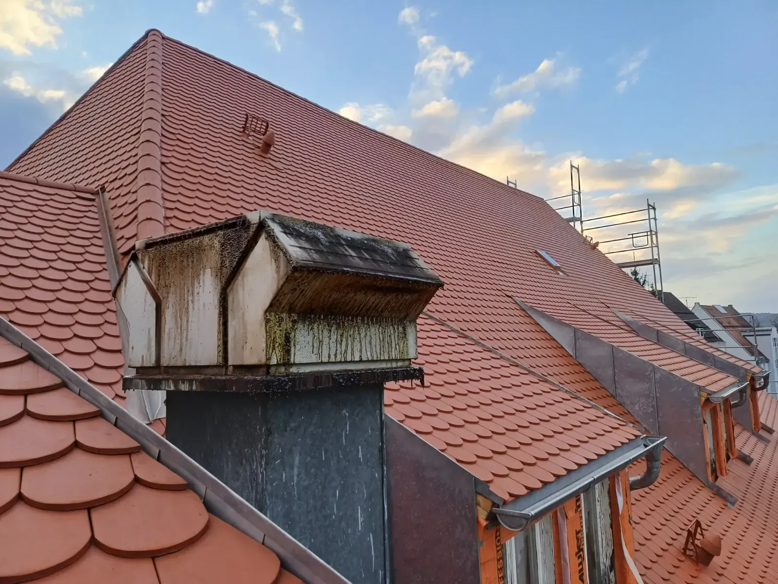 Rotes Ziegeldach mit verwitterten Dachgauben vor einem bewölkten Himmel