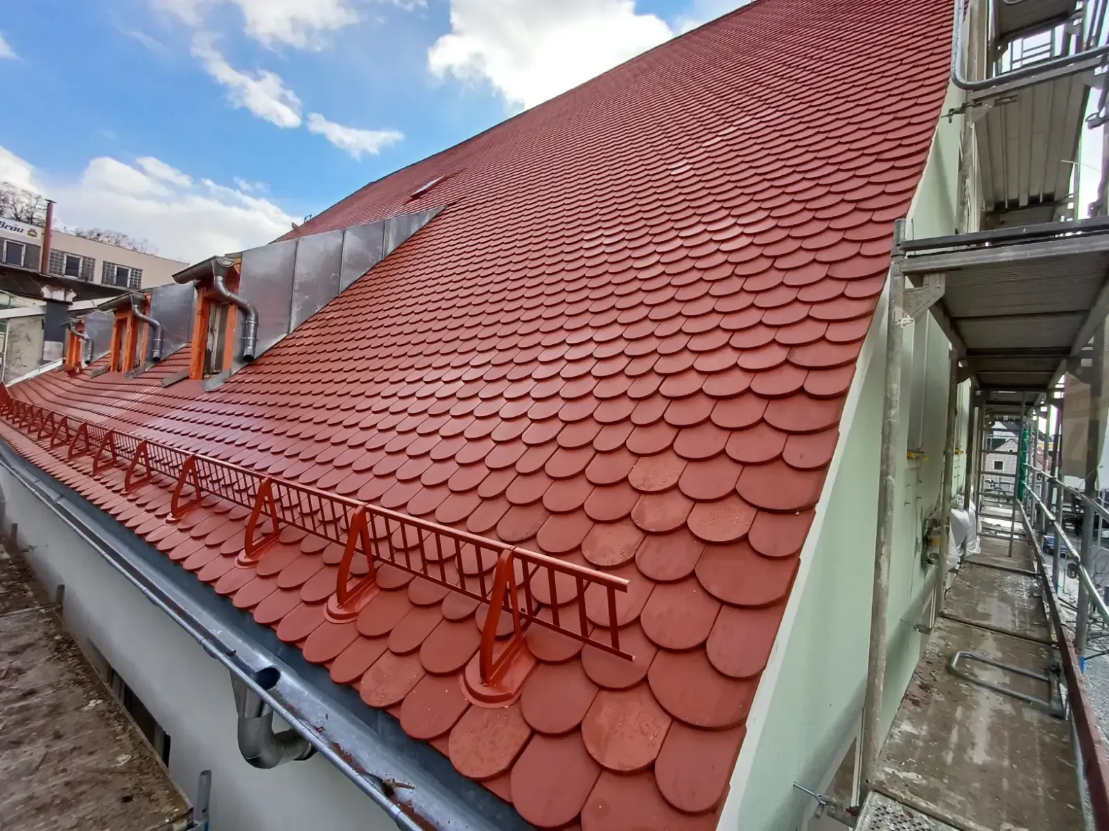 Ein im Bau befindliches rotes Ziegeldach mit Arbeitern und Gerüsten entlang der Traufe.
