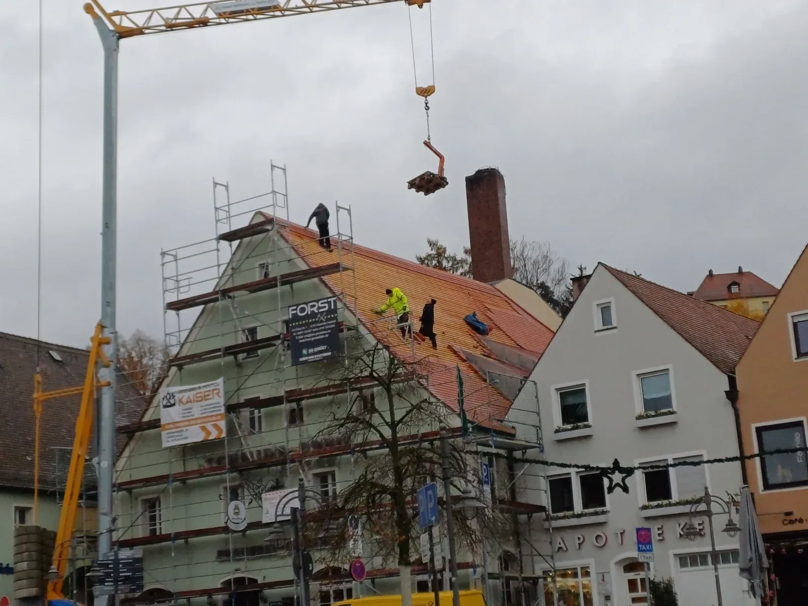 Arbeiter auf einem Gerüst reparieren unter einem Kran das Dach eines Hauses in einer bewölkten Stadtstraße.