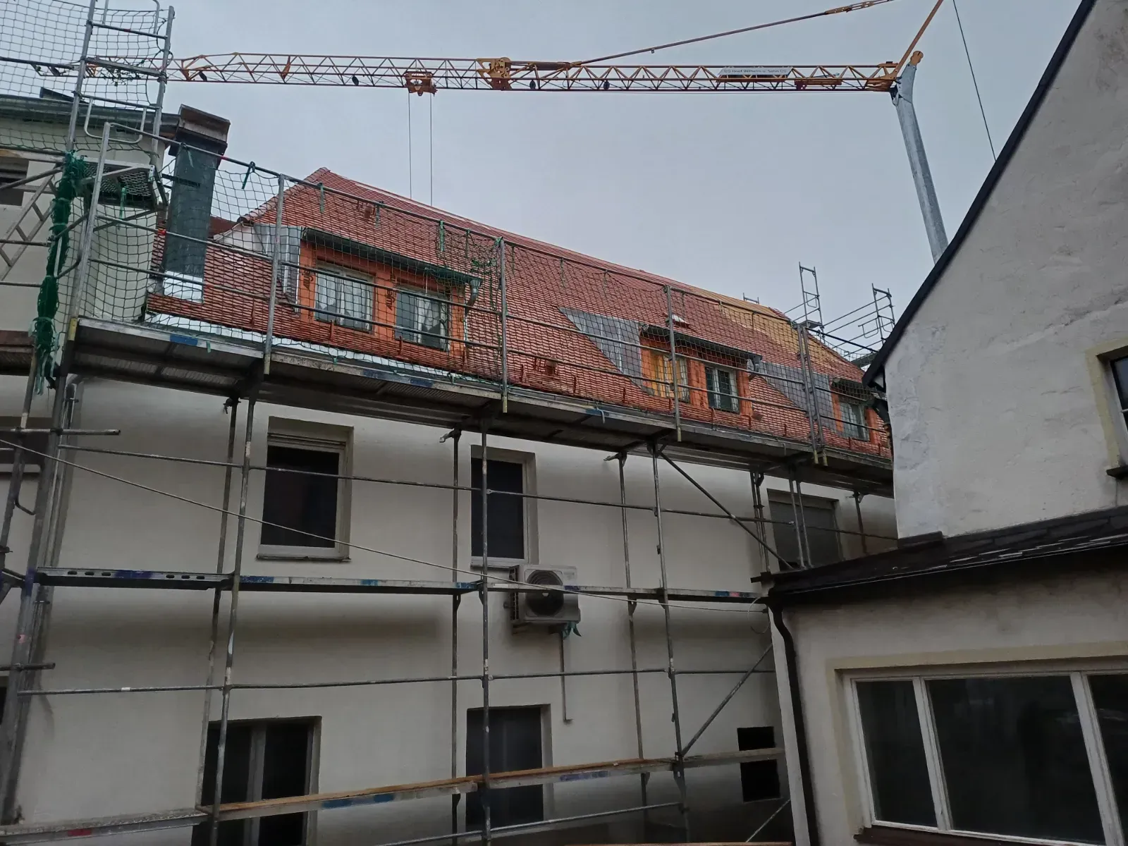 Ein Gerüst umgibt ein weißes Gebäude mit rotem Ziegeldach in einem Innenhof.