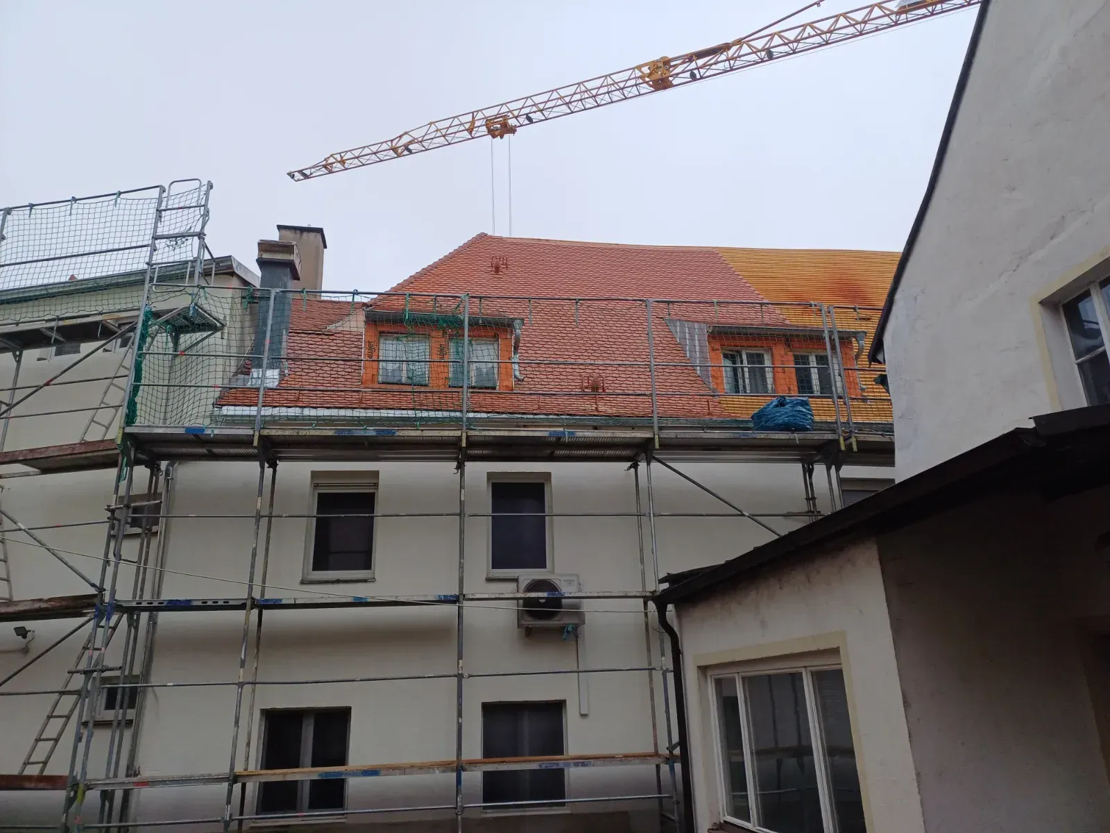 Gebäude im Umbau mit Gerüst, orangefarbenem Ziegeldach und einem Kran darüber