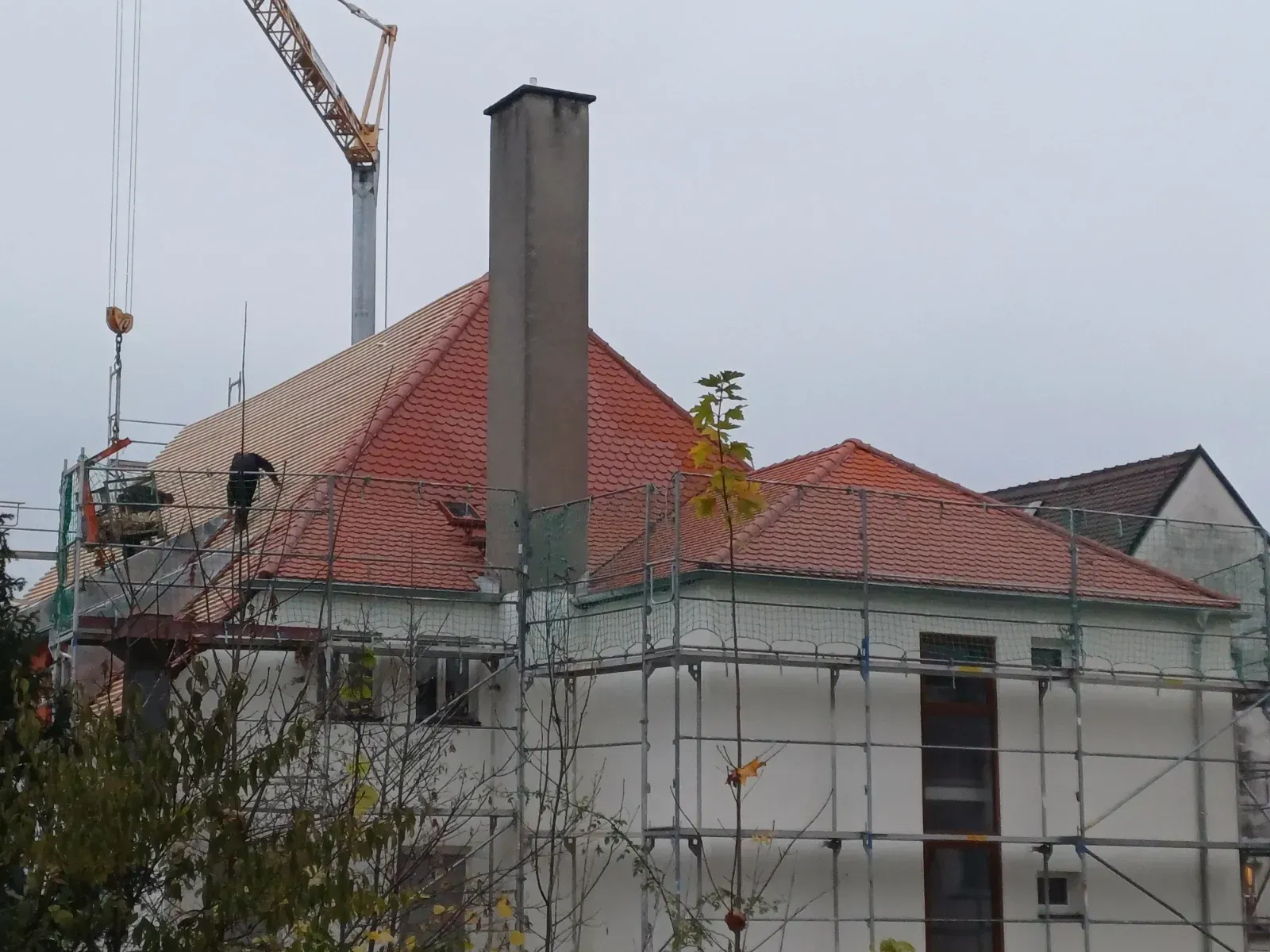 Haus im Bau mit rotem Ziegeldach, Gerüst und einem Kran darüber
