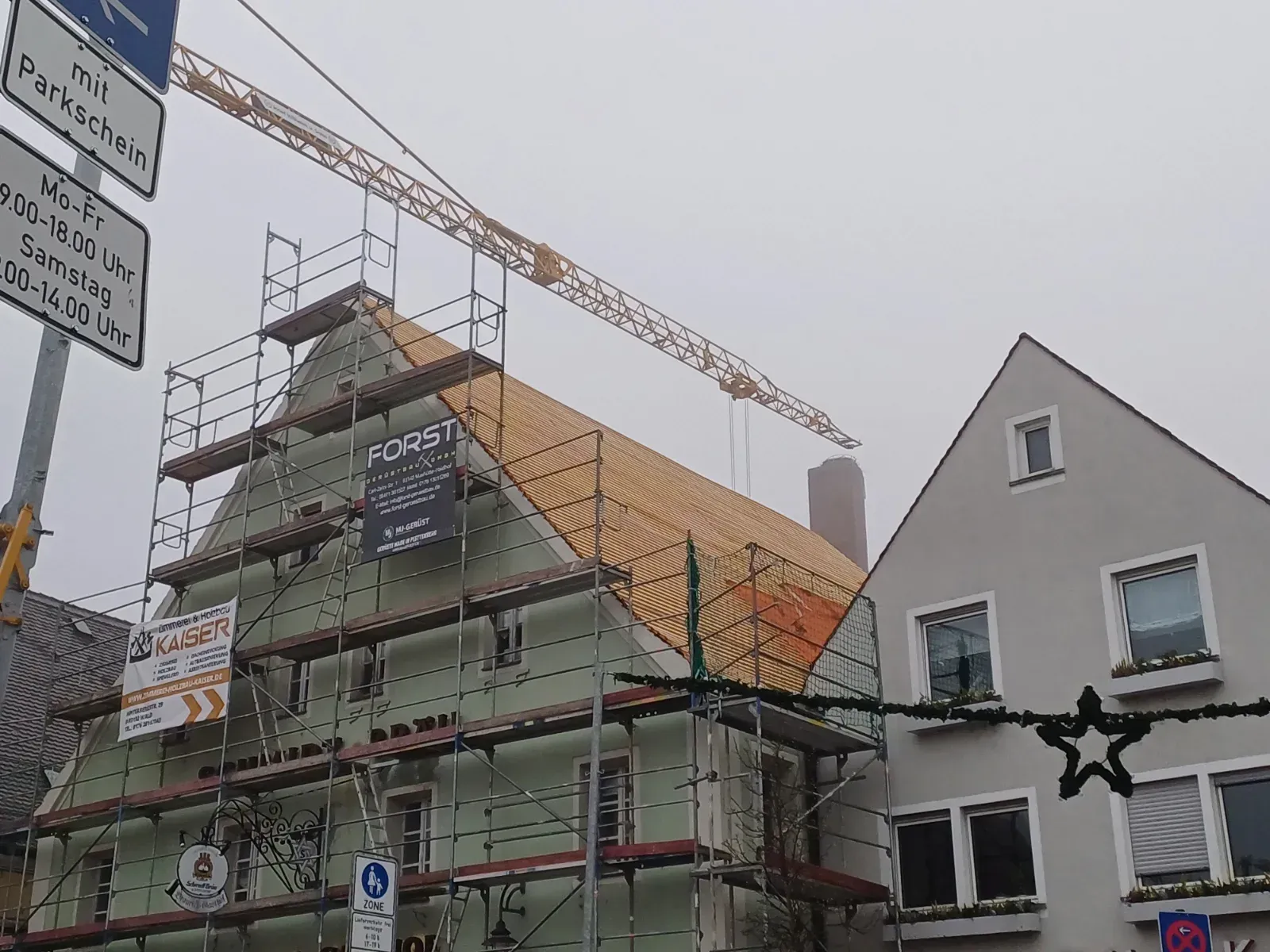 Neben einem weißen Haus an einer Straßenecke befindet sich ein im Bau befindliches Gerüst.