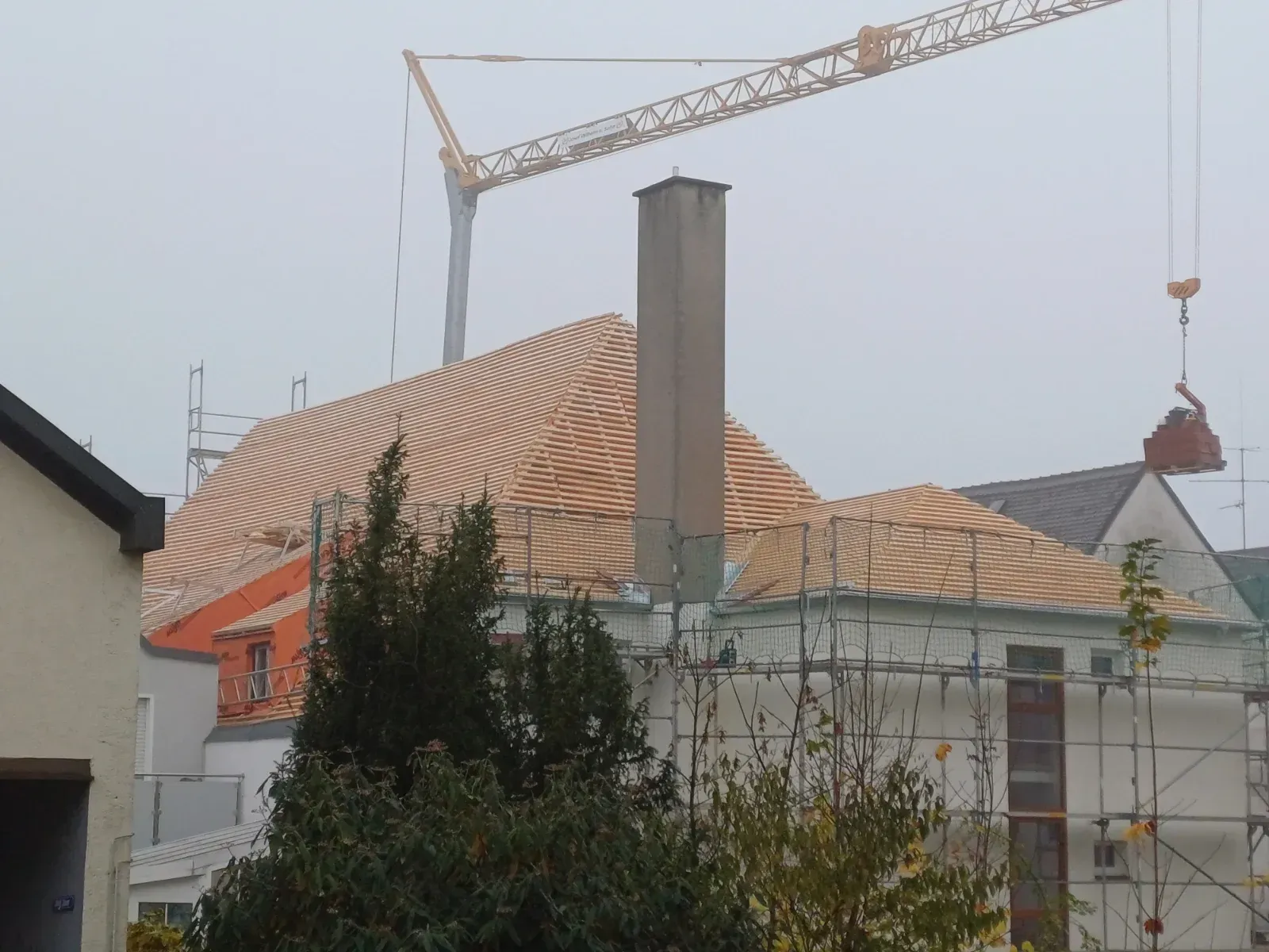 Baustelle mit Kran neben Häusern und einem eingerüsteten Dach, das repariert wird