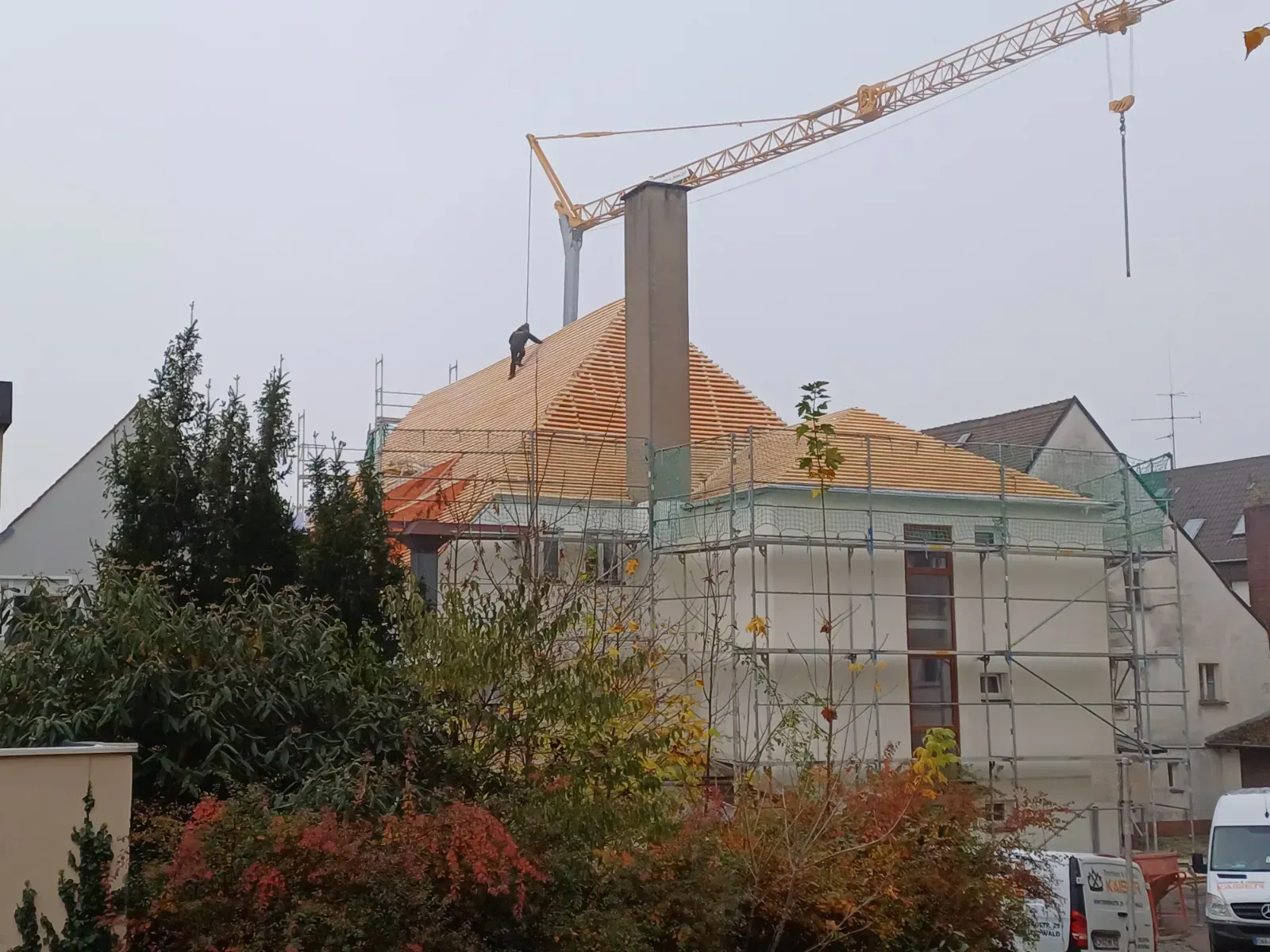 Ein Kran über einem im Bau befindlichen Haus mit orangefarbenen Dachziegeln und Gerüst in einem Wohngebiet