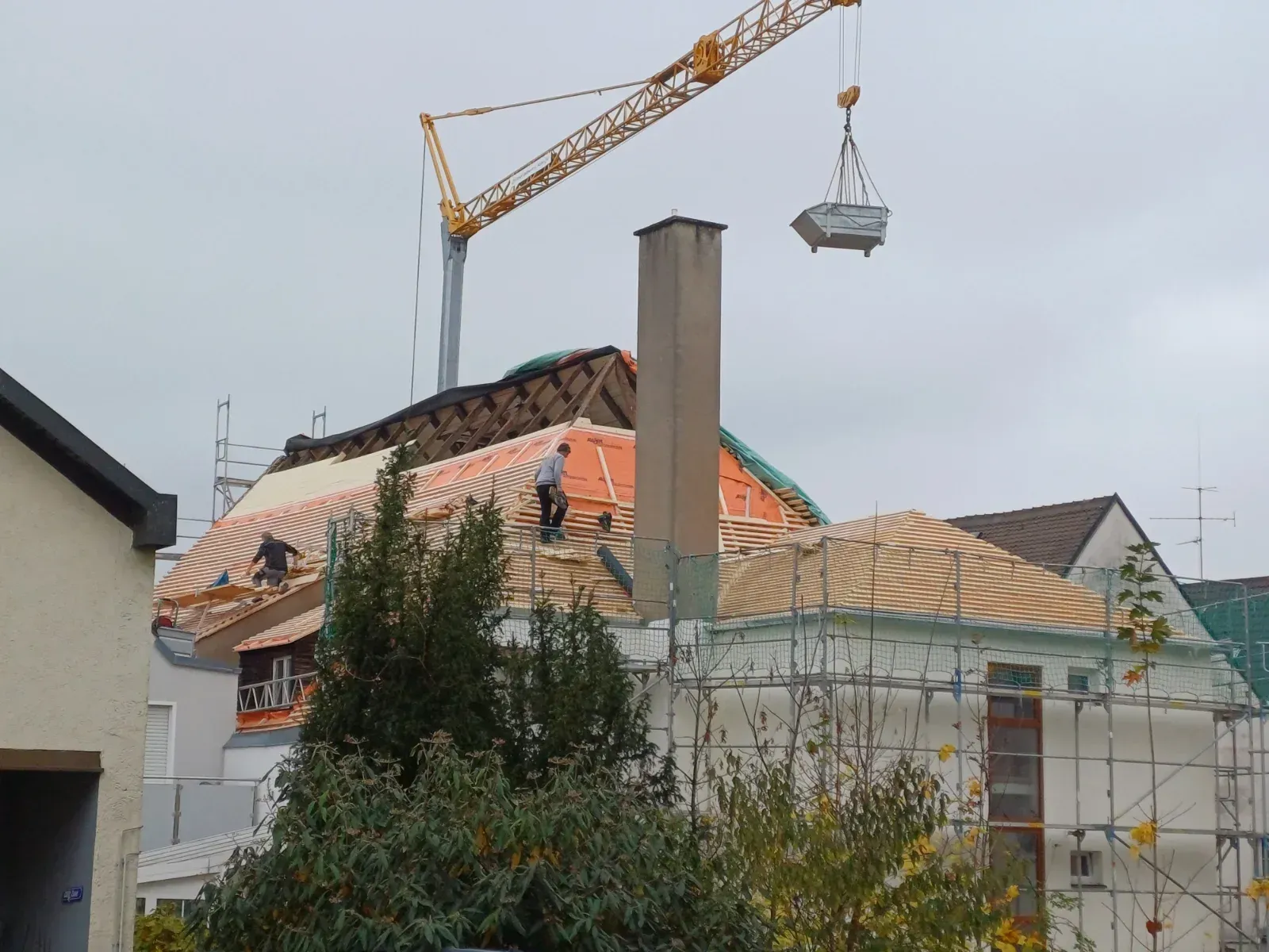 Haus im Umbau mit Dachziegeln, Gerüst und einem Kran, der darüber Baumaterialien hebt